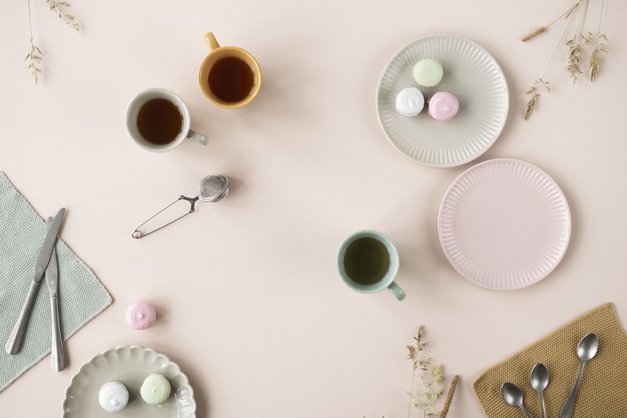 Zwei Tassen mit Getränken, mehrere Teller mit bunten Macarons, Besteck und eine Serviette auf einem hellen Tisch.