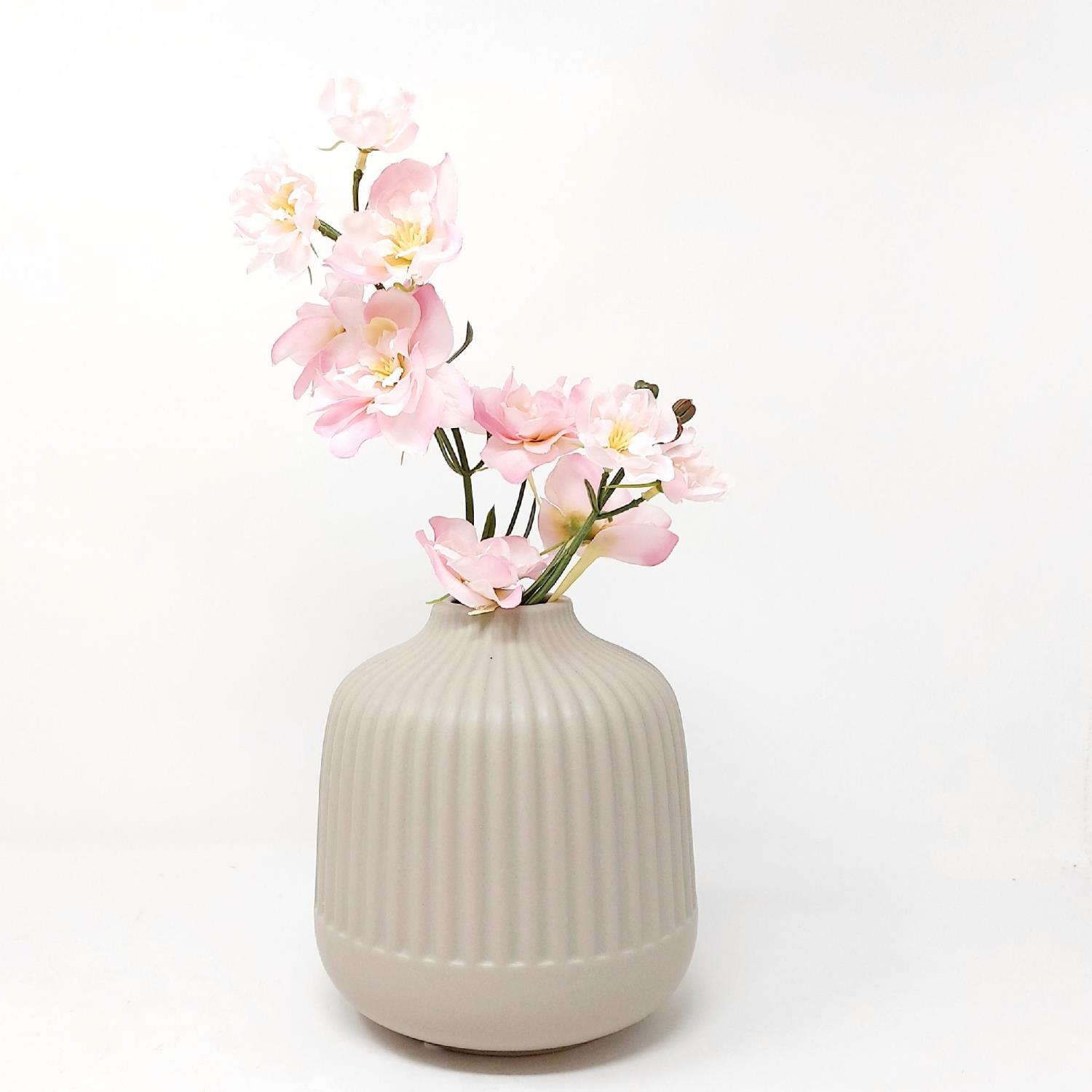 Eine beige, gerippte Vase mit rosa Blumen steht vor einem weißen Hintergrund.