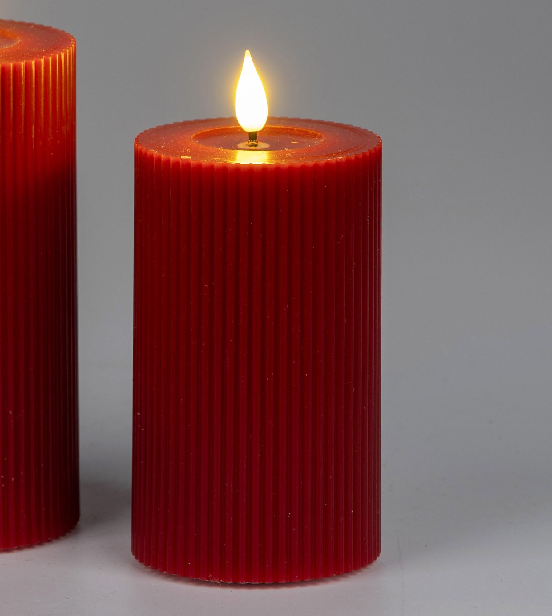 Zwei rote Kerzen mit gerillter Oberfläche, eine brennt mit einer kleinen Flamme auf der Oberseite. H
