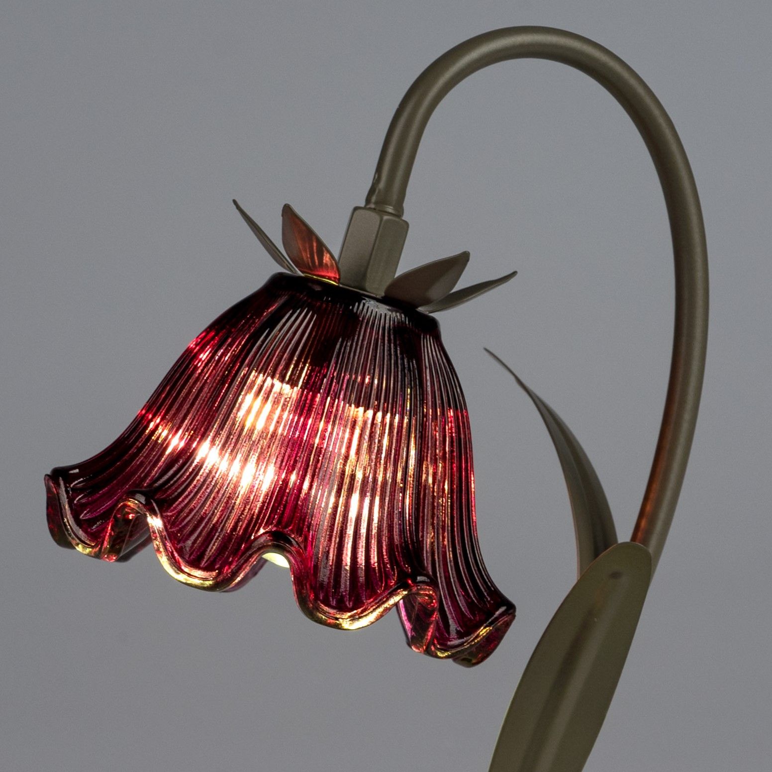 Eine Tischlampe mit einem blütenförmigen, rot-transparenten Lampenschirm und einem geschwungenen Met