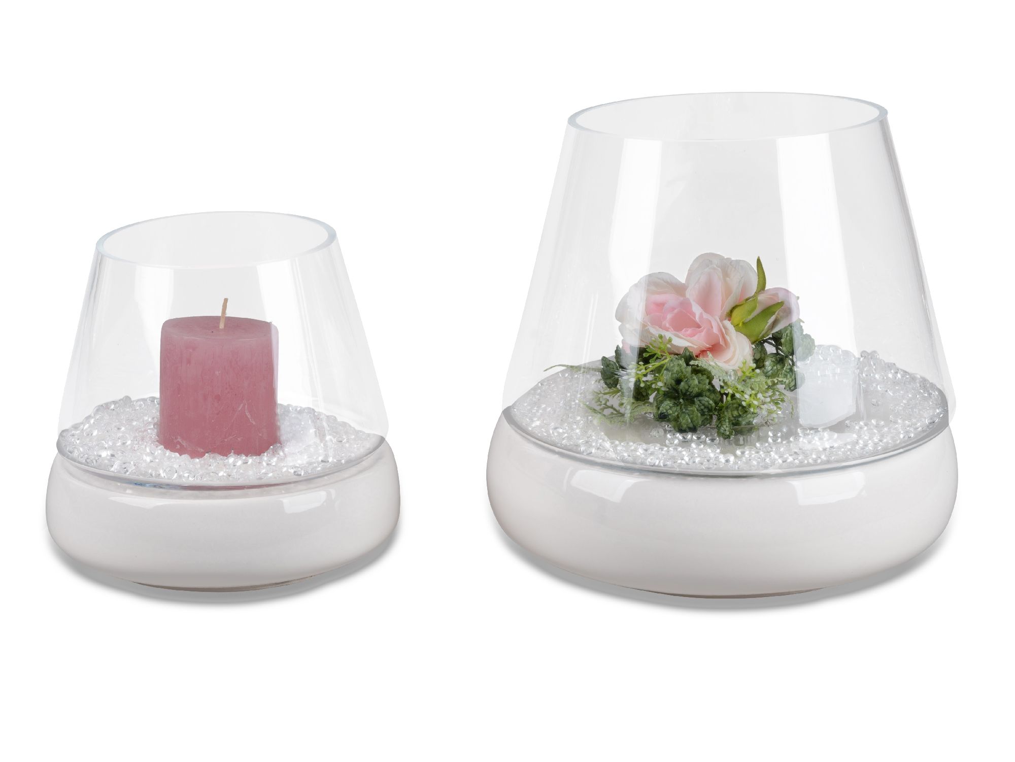 Zwei Glasbehälter mit einer Kerze und einer Blumendekoration auf weißem Untergrund, gefüllt mit kleinen weißen Perlen.