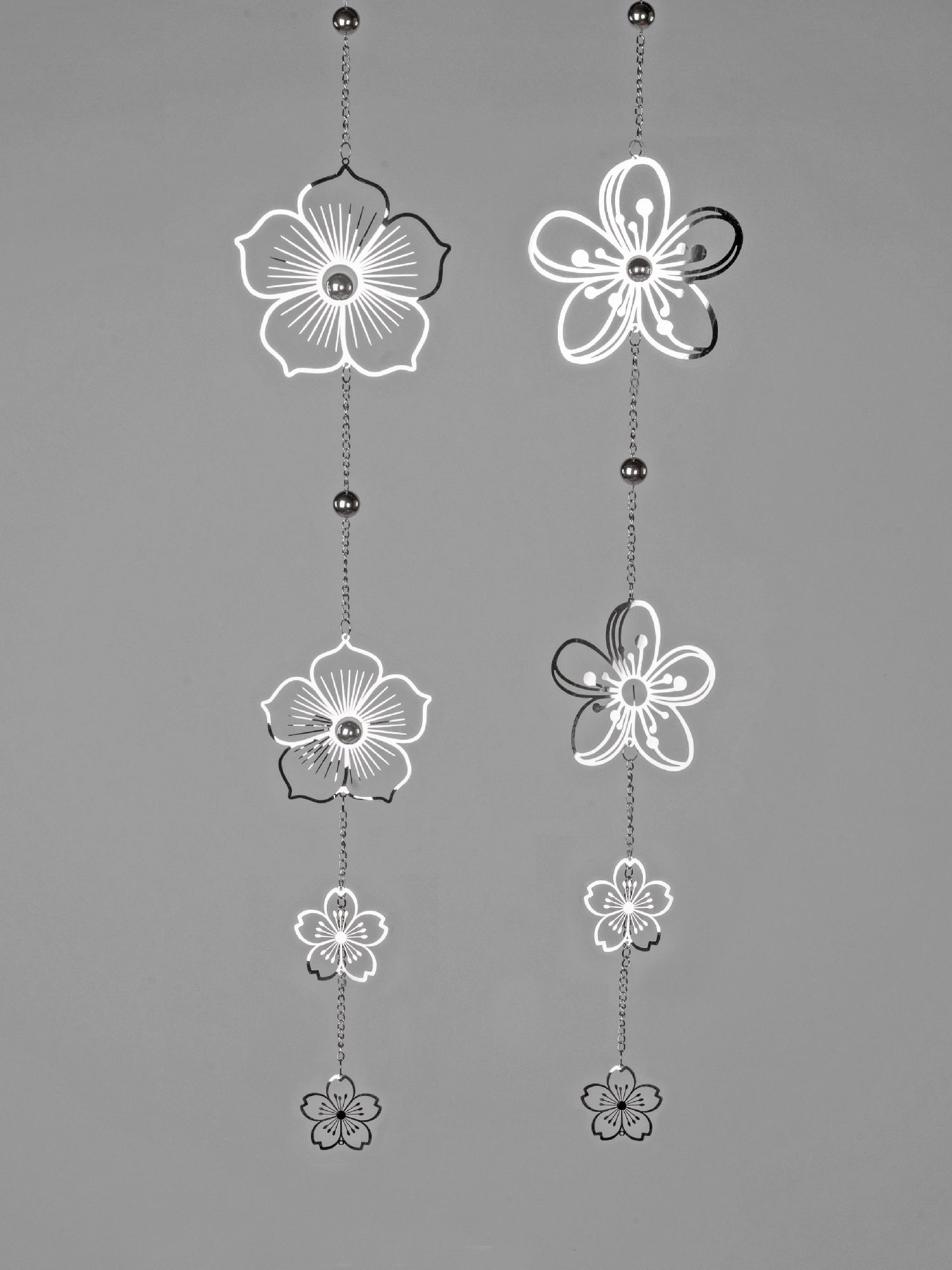 Zwei hängende Dekorationen mit floralen Motiven in Schwarz und Weiß, die an Ketten befestigt sind. Hintergrund in Grau.