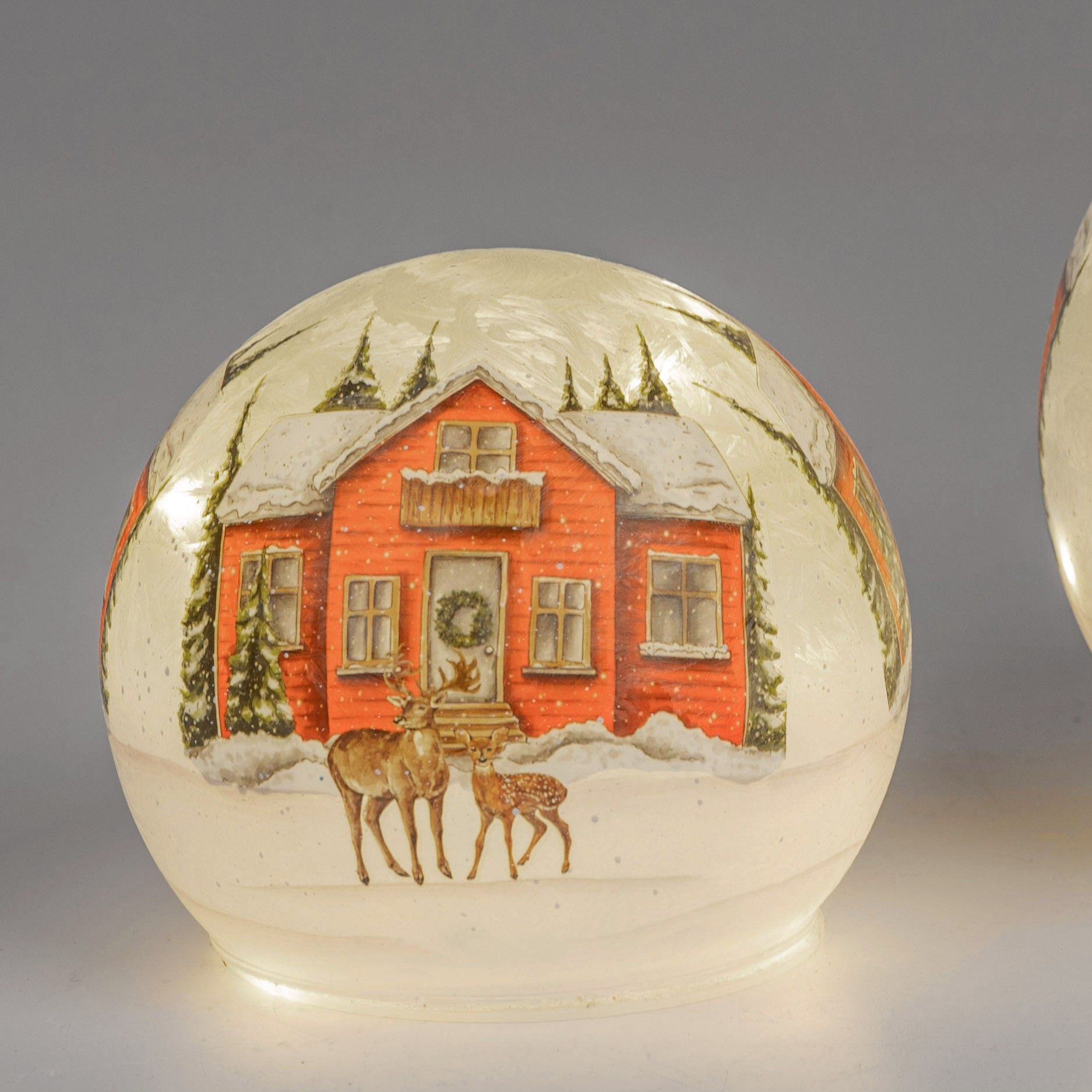 Eine rot gestrichene Hütte im Schnee, umgeben von Tannen, mit zwei Rehen im Vordergrund.