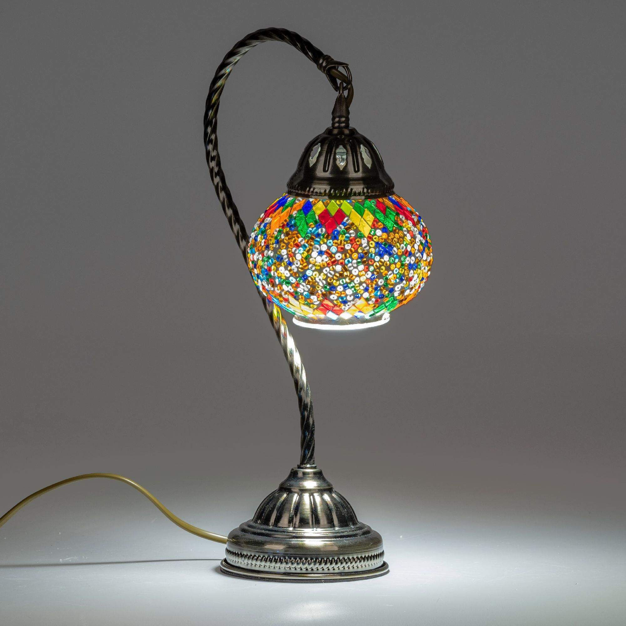 Bunte Tischlampe mit gläsernem Lampenschirm und verziertem Metallfuß, leuchtet sanft in einem neutra