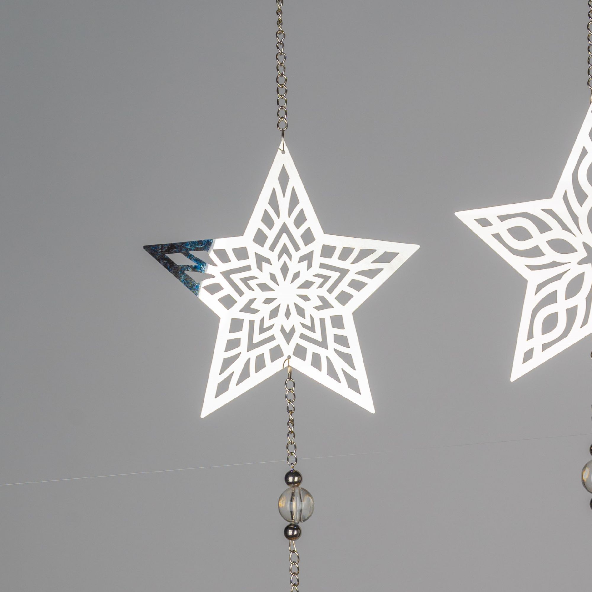 Zwei hängende, filigrane, weiße Sterne mit geometrischen Mustern und einer Kette aus Perlen im Hinte