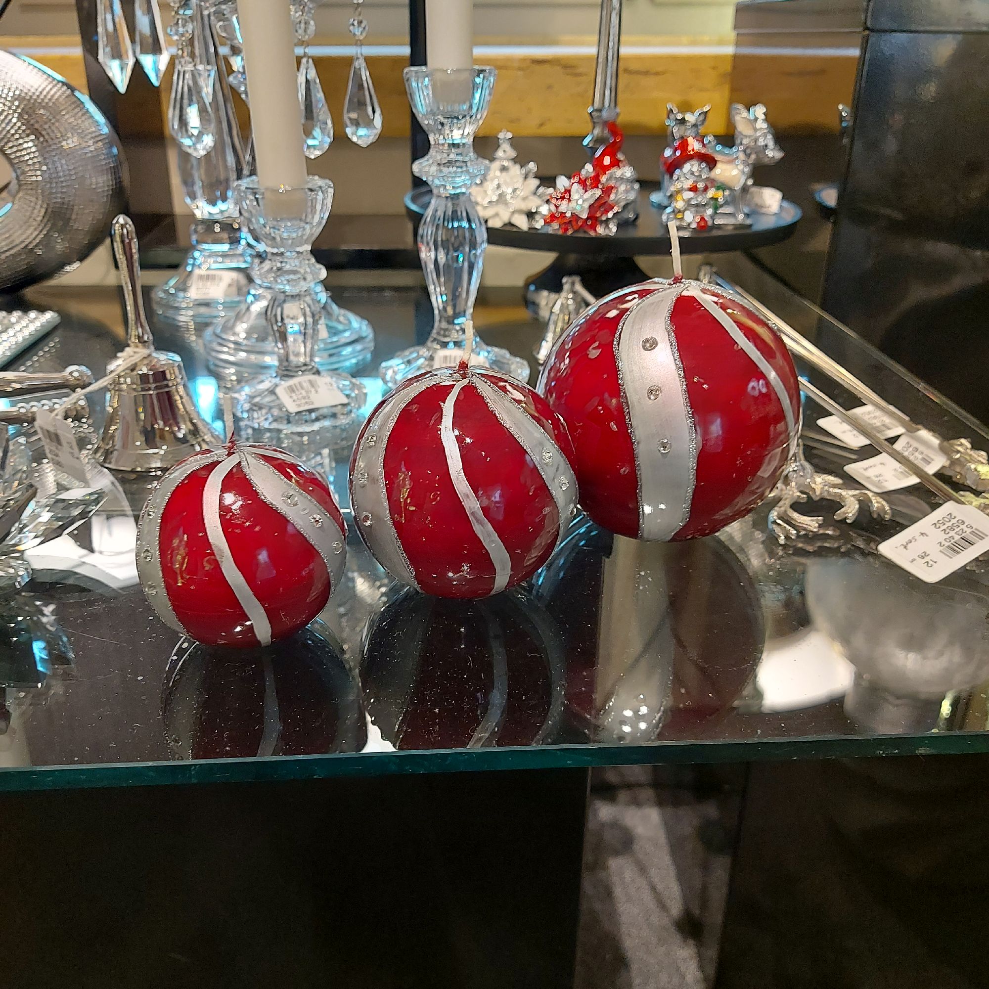 Drei rote Kugeln mit silbernen Streifen und Glitzer stehen auf einem Tisch, umgeben von weiteren dek