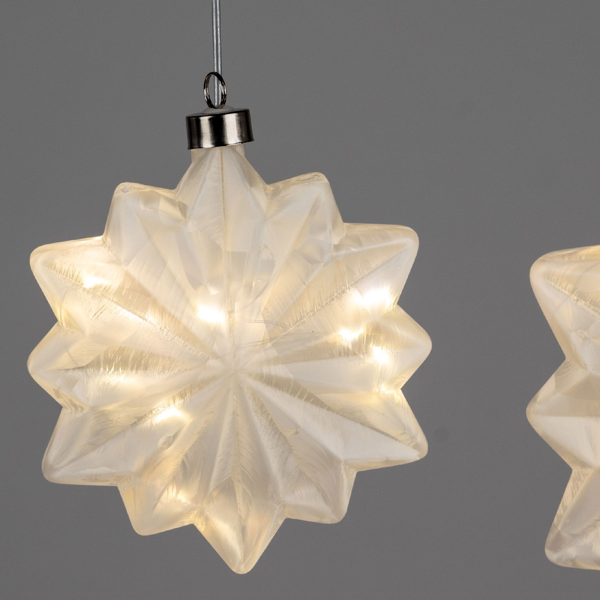 Hängende, durchsichtige Sternlichter mit warmem Licht auf grauem Hintergrund. Zwei Sterne sind sicht