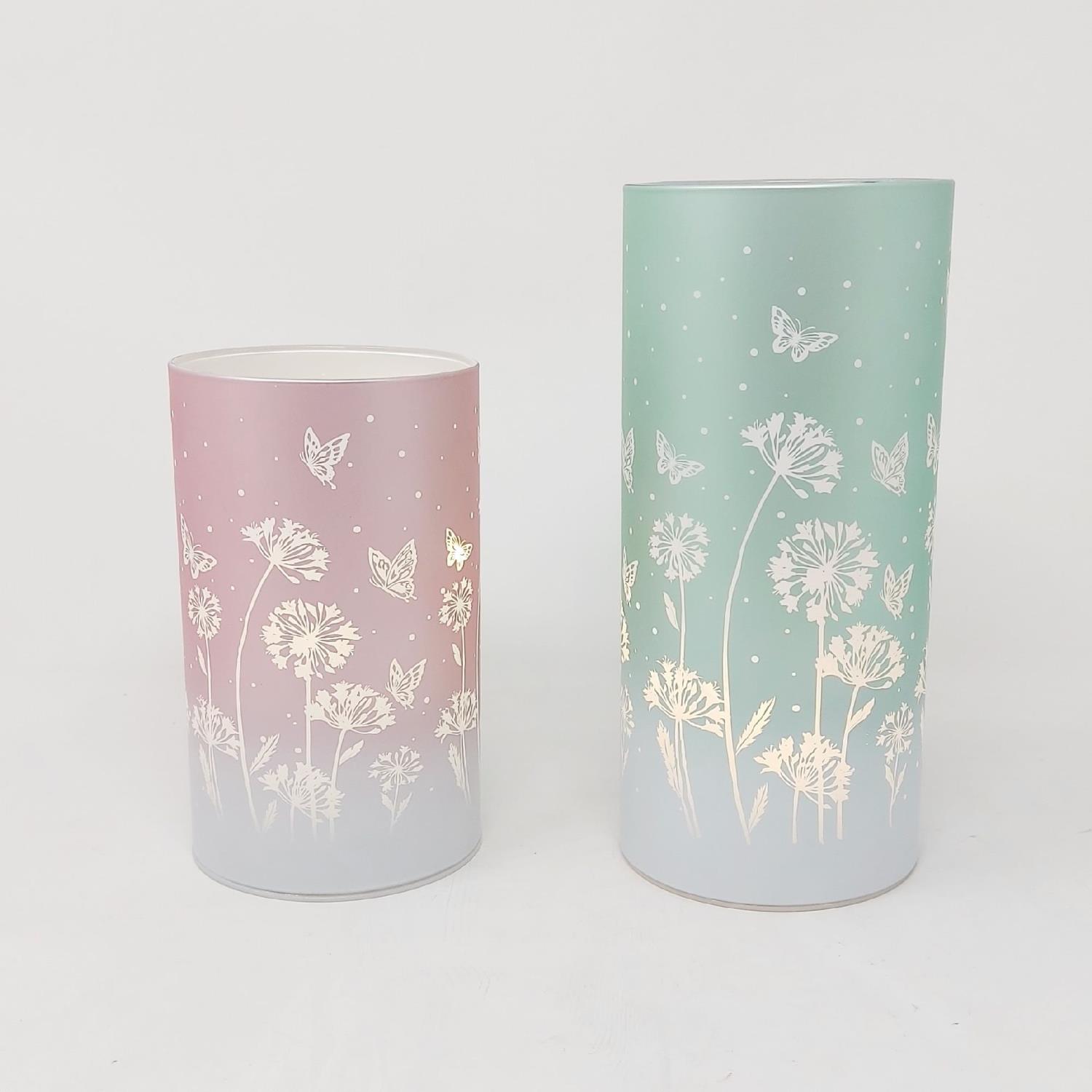 Zwei zylindrische Behälter in Rosa und Grün mit floralem Muster und Schmetterlingen auf hellem Hintergrund.