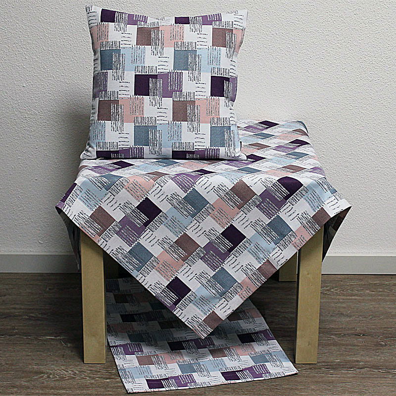 Ein Tisch mit einer gemusterten Tischdecke und einem passenden Kissen. Das Muster besteht aus bunten, geometrischen Formen.