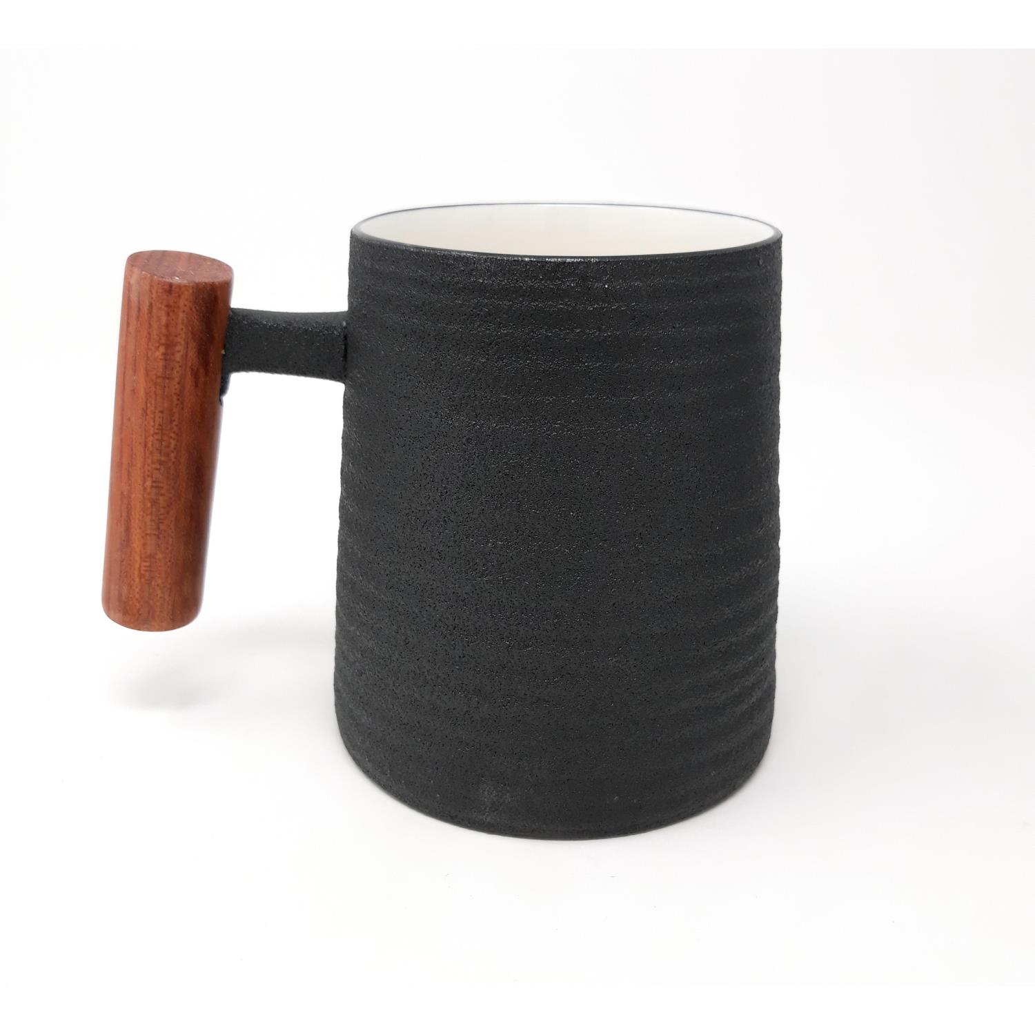 Schwarze Tasse mit strukturiertem Außenbereich und Holzgriff, innen weiß. Steht auf einem hellen Untergrund.
