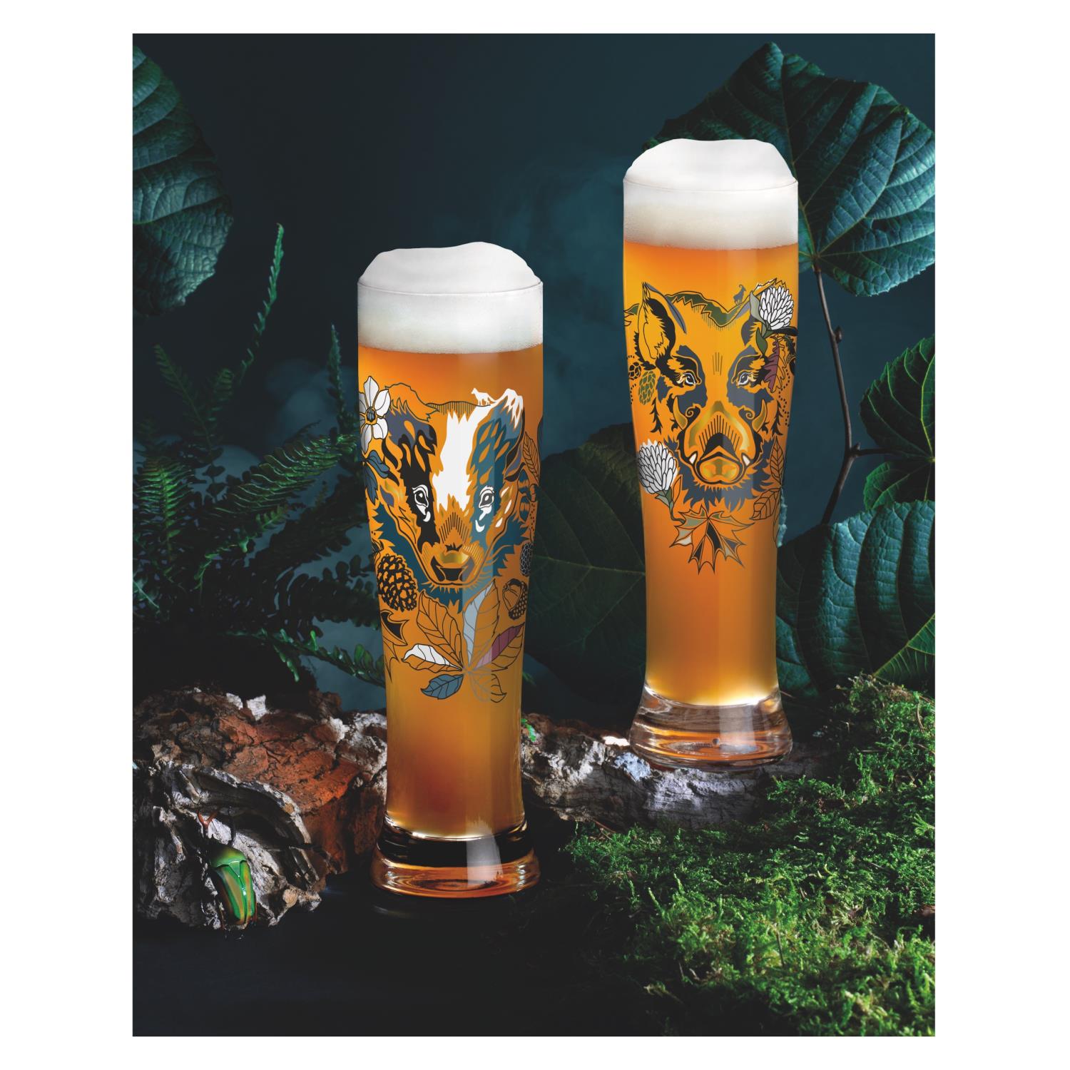 Zwei Gläser mit Bier, verziert mit Tiermotiven, stehen auf einer Holzoberfläche umgeben von Pflanzen und Moos.