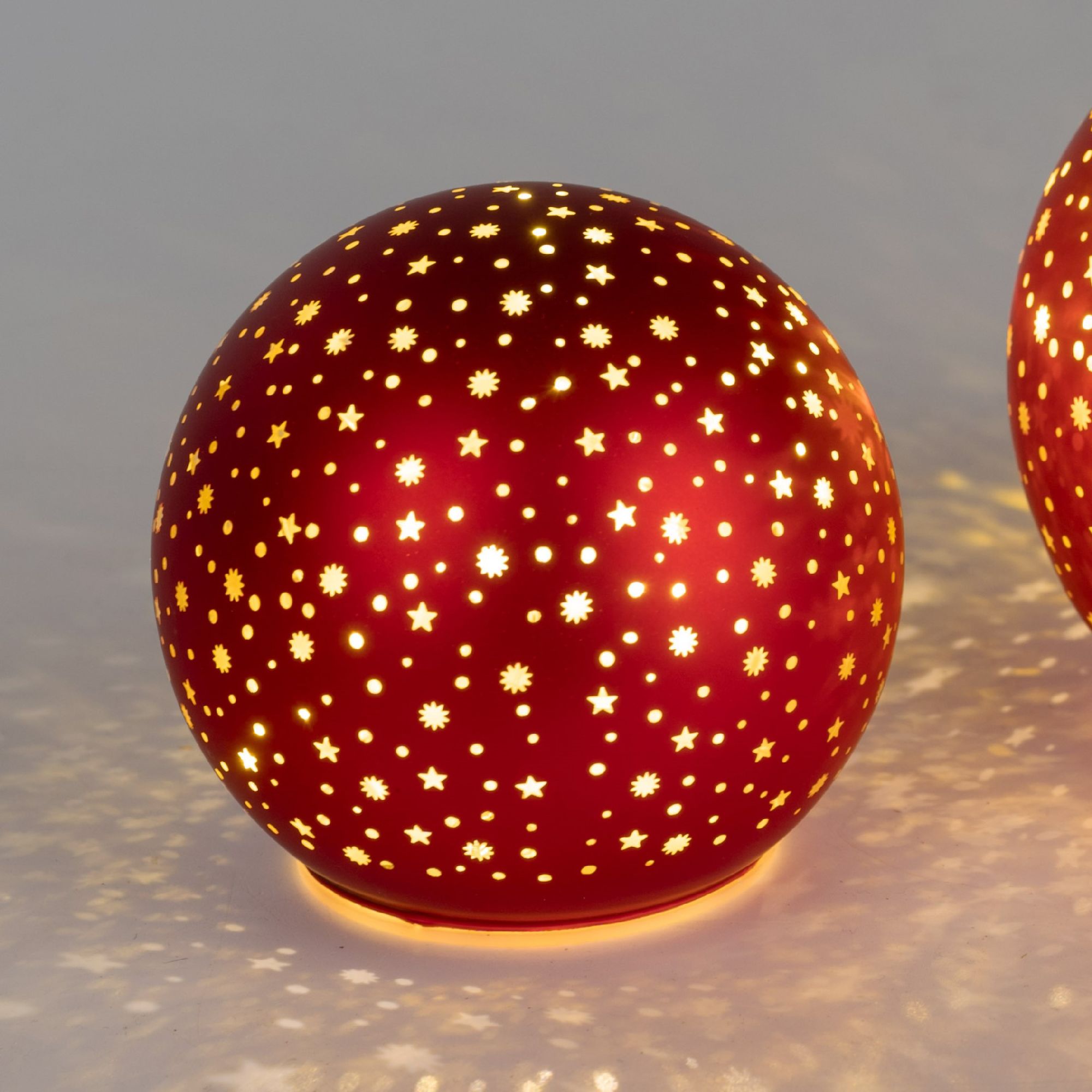 Runde, rote Leuchte mit durchbrochenem Muster aus Sternen und Blumen, die warmes Licht abstrahlt und