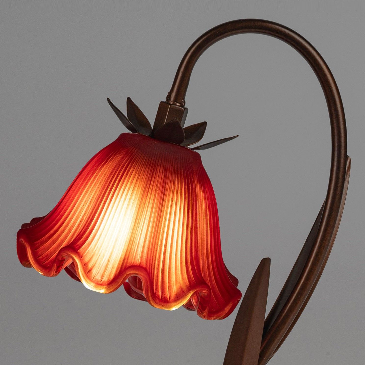 Eine Tischlampe mit einem rot gefärbten, blütenförmigen Lampenschirm und einem geschwungenen Metallg