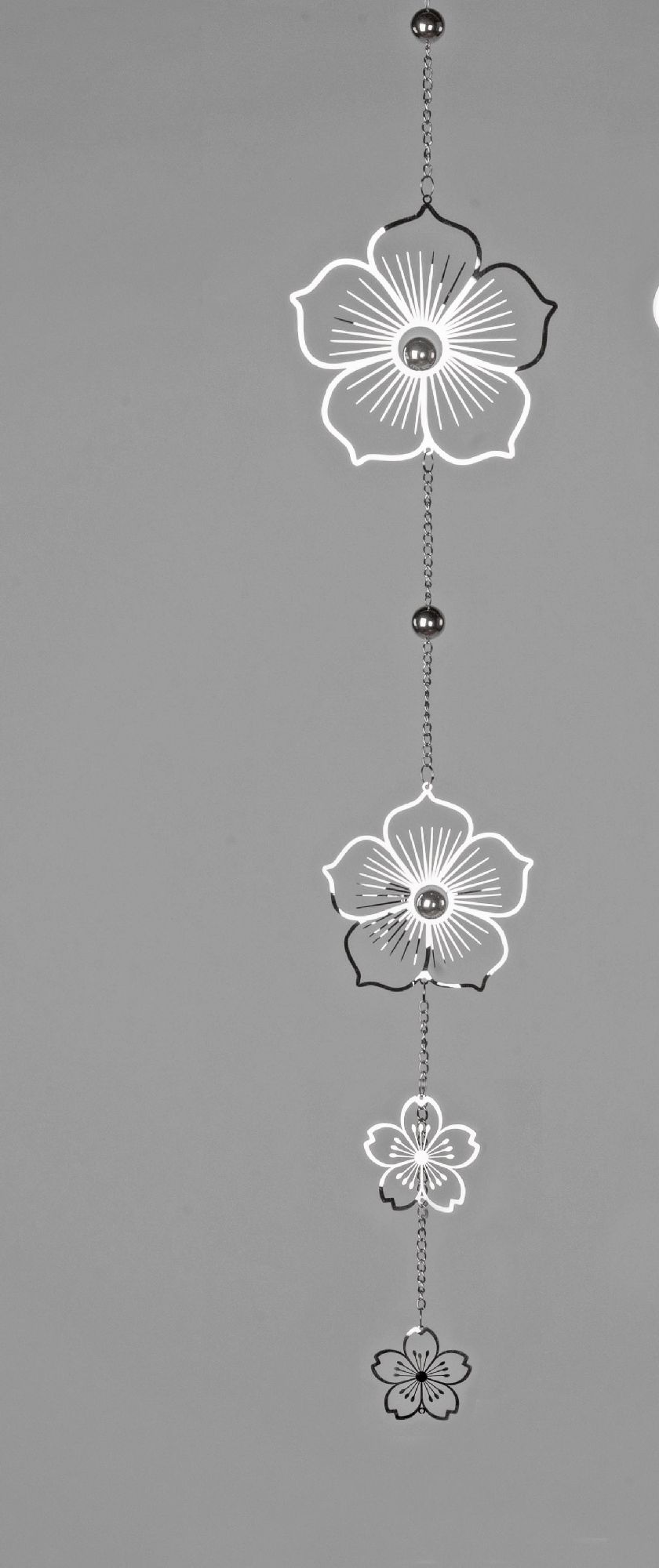 Hängende Dekoration mit mehreren stilisierten Blumen in Schwarz und Weiß, verbunden durch eine Kette, vor grauem Hintergrund.