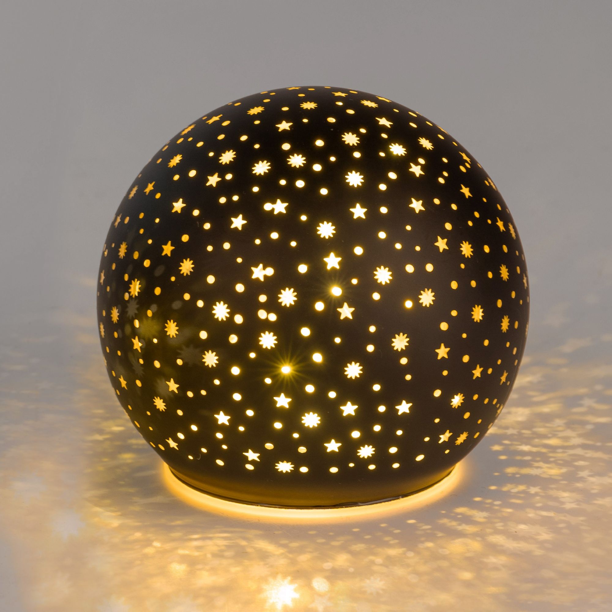 Runde Lampe mit perforierter Oberfläche, die warmes Licht ausstrahlt und ein Muster aus Sternen und