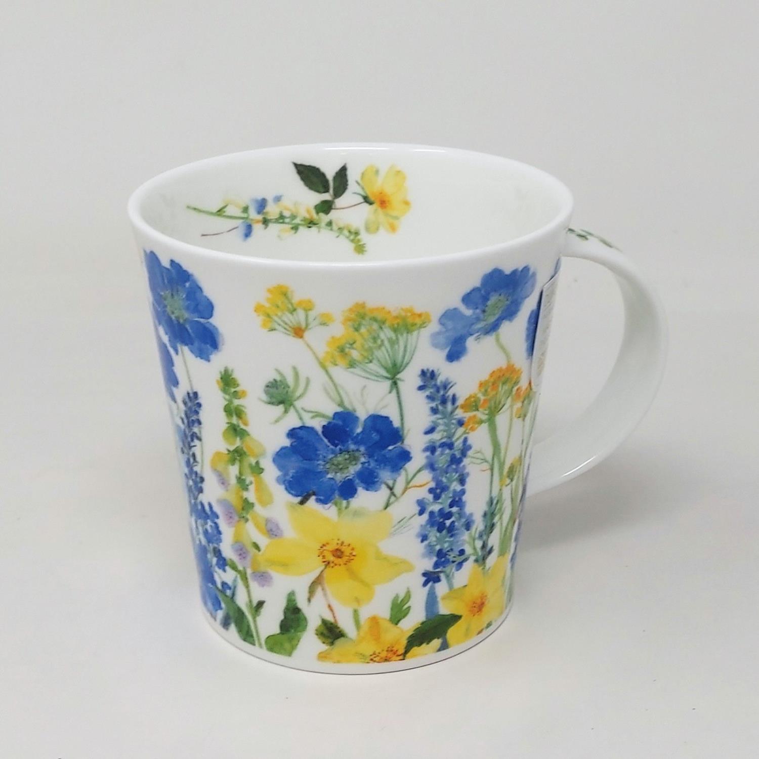 Weißer Becher mit buntem Blumenmuster in Blau, Gelb und Grün. Der Becher hat einen Henkel und ist auf einem hellen Hintergrund platziert.