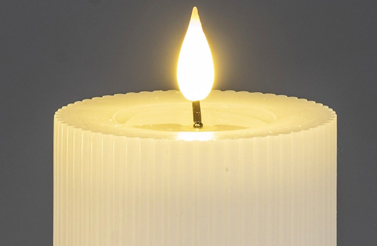 Eine weiße Kerze mit einer flackernden Flamme auf einem grauen Hintergrund. Die Kerze hat eine gerillte Oberfläche.