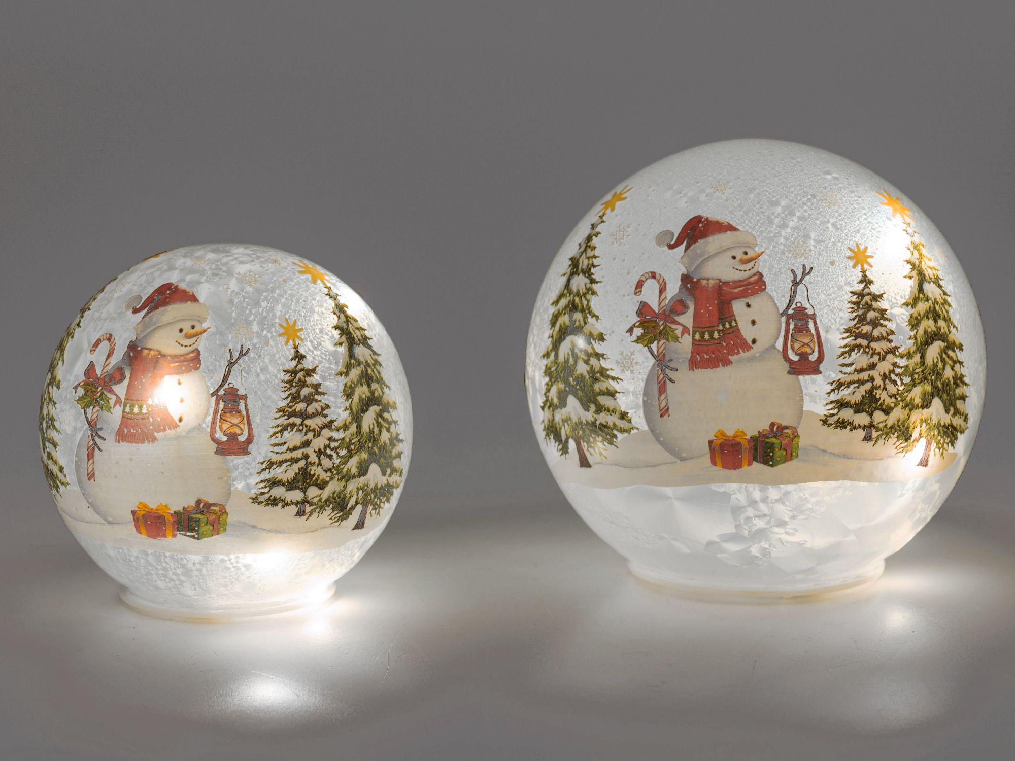 Zwei Kugellampen mit Schneemann, Tannenbäumen und Geschenken auf dunklem Hintergrund