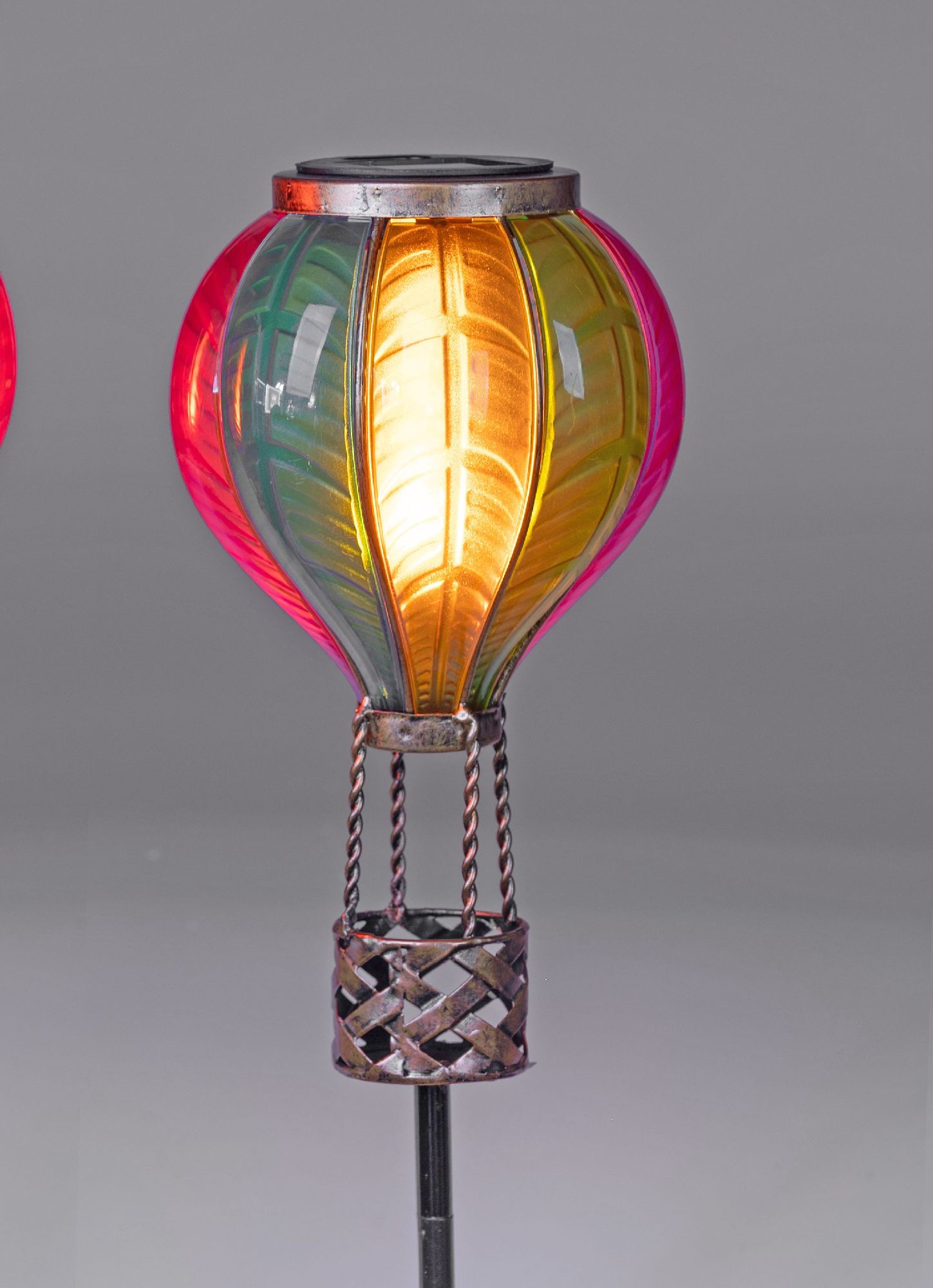 Bunte Laterne in Form eines Heißluftballons mit metallischem Korb, leuchtet in verschiedenen Farben auf grauem Hintergrund.