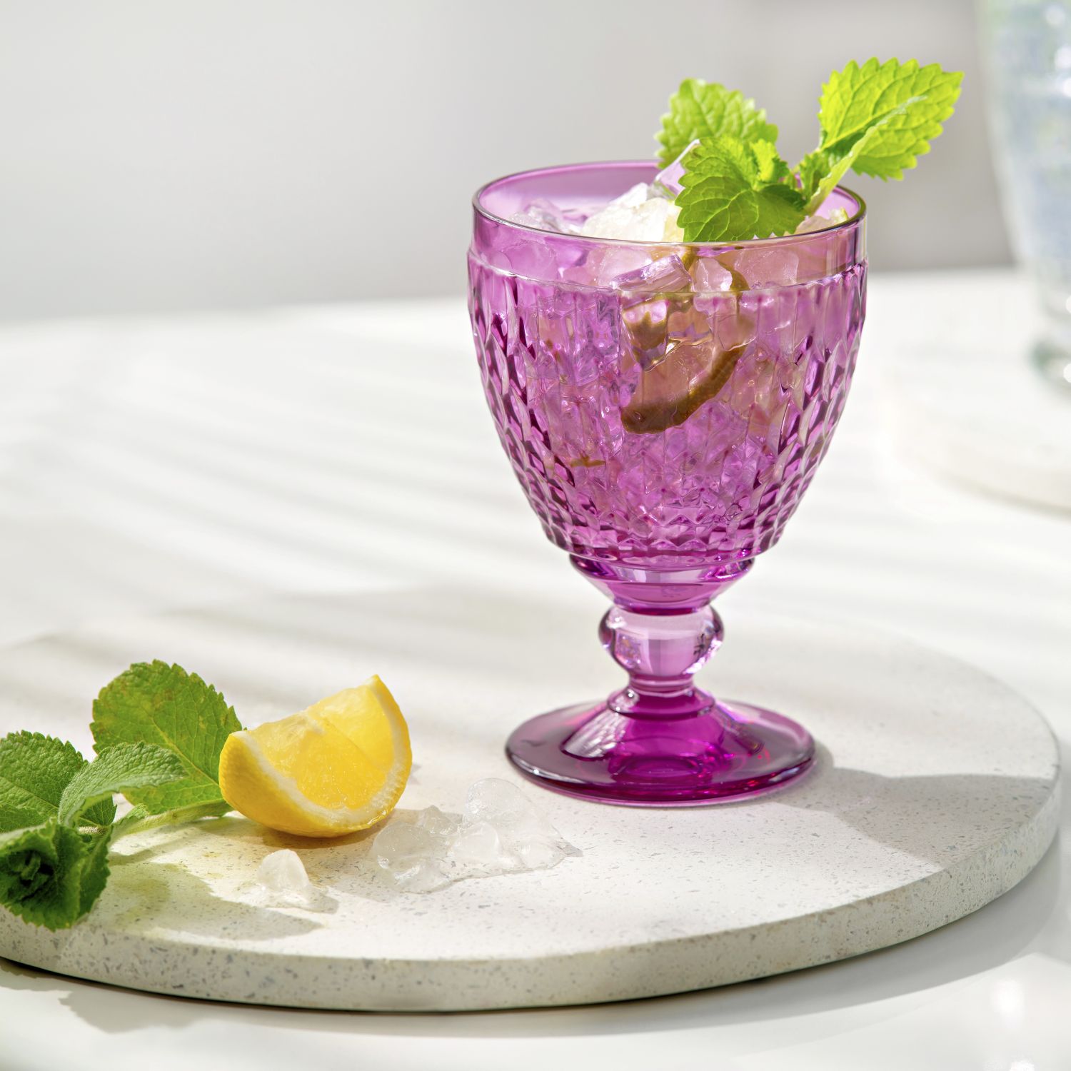 Ein lila Glas mit Eis, Minze und einer Zitronenscheibe auf einem weißen Untersetzer