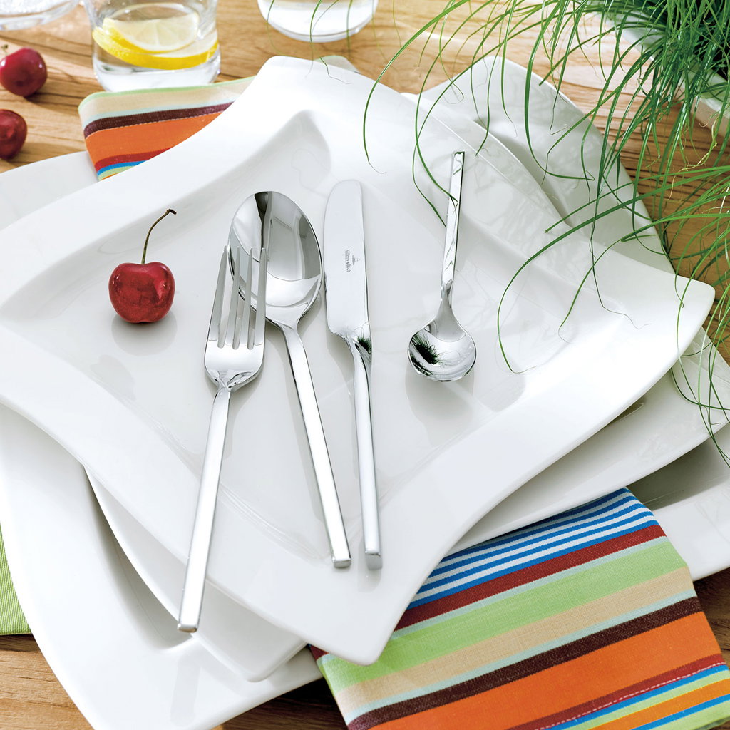 Ein gedeckter Tisch mit weißen Tellern, Besteck (Gabel, Messer, Löffel) und einer Kirsche. Bunte Ser