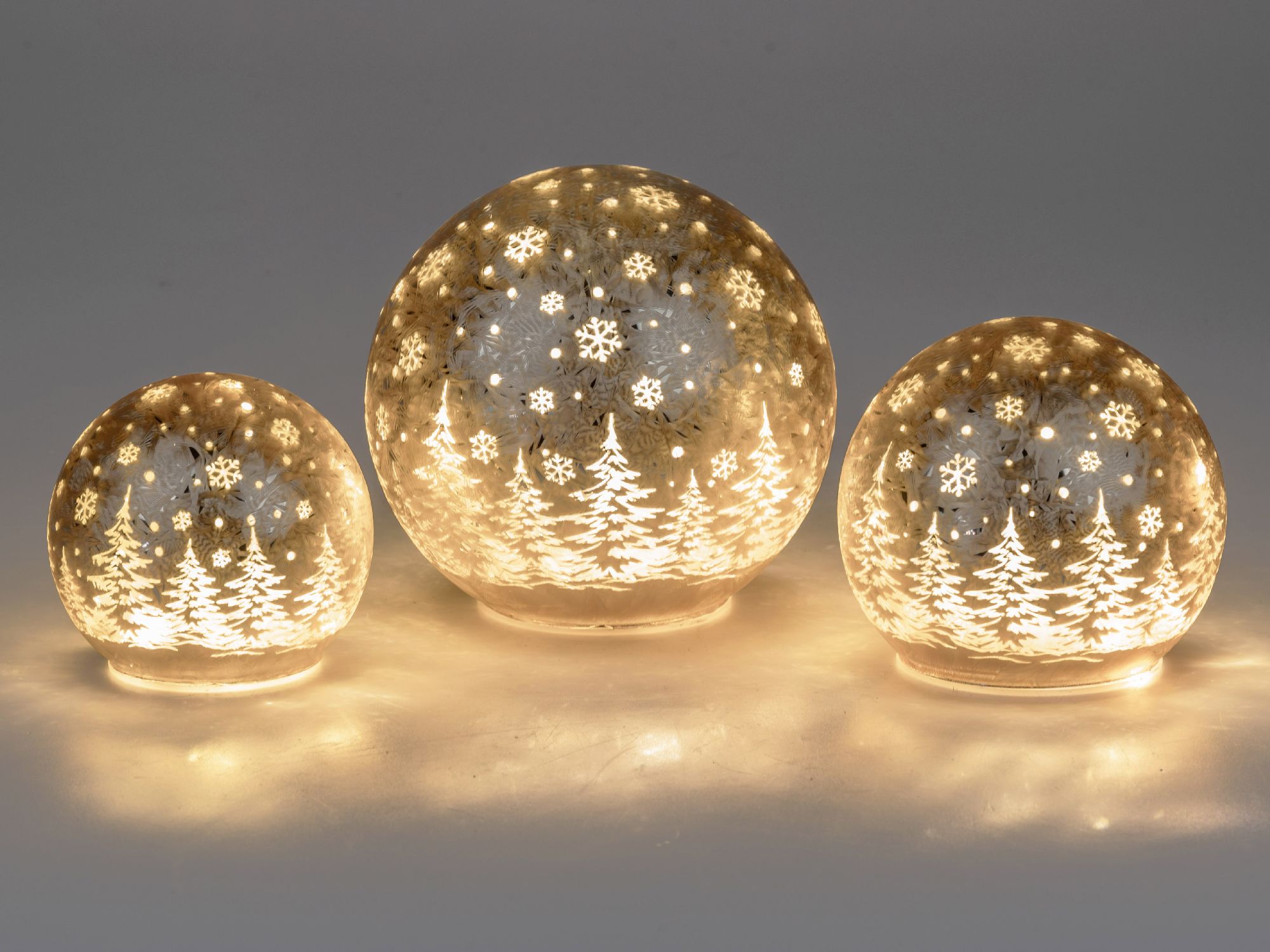 Drei leuchtende Glaskugeln in verschiedenen Größen mit winterlichen Motiven von Tannenbäumen und Sch