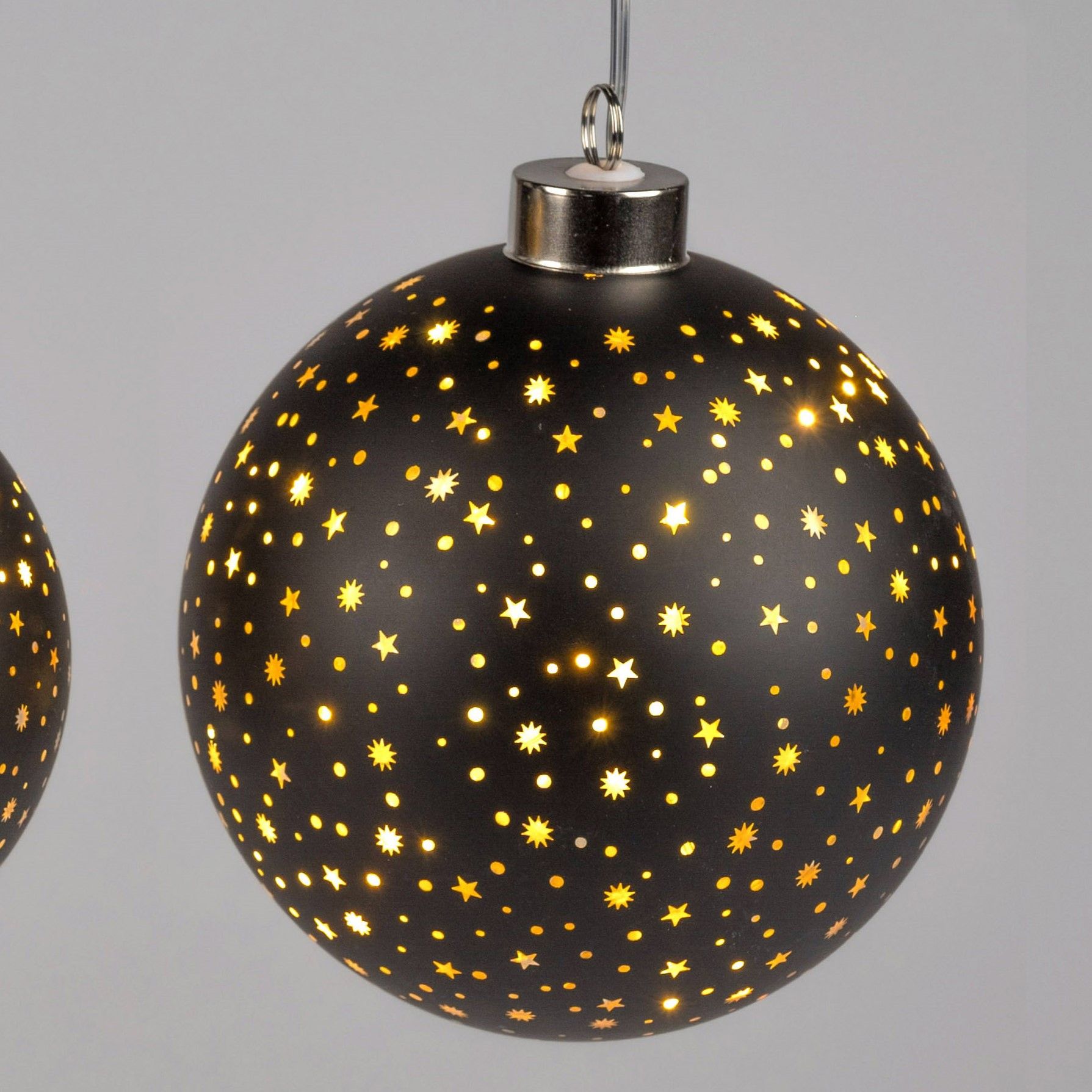 Schwarze Weihnachtskugel mit goldenen Sternen und kleinen Löchern, die Licht durchlassen, hängt an e