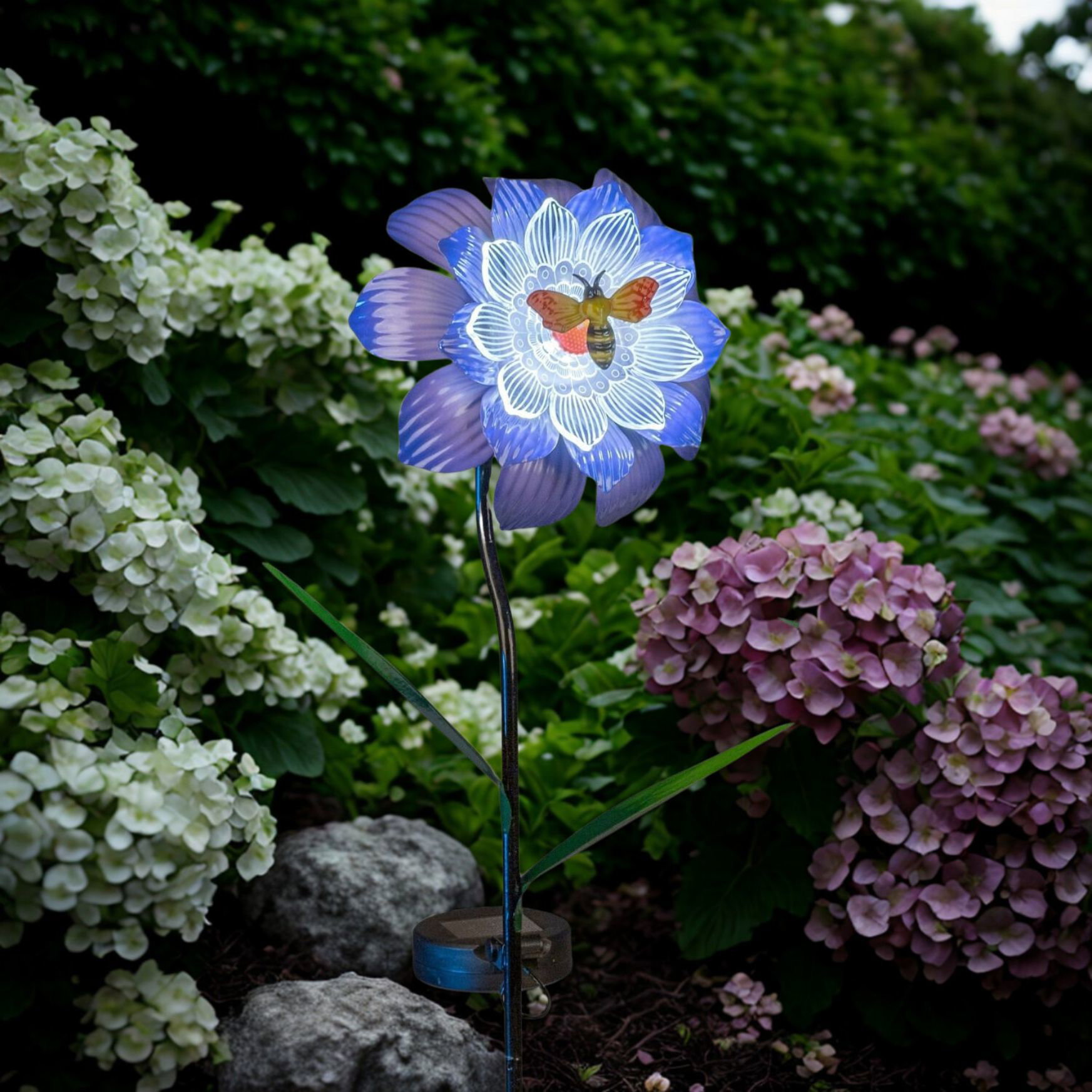 Dekorative blaue Blume mit leuchtendem Muster im Garten zwischen Hortensien und Steinen