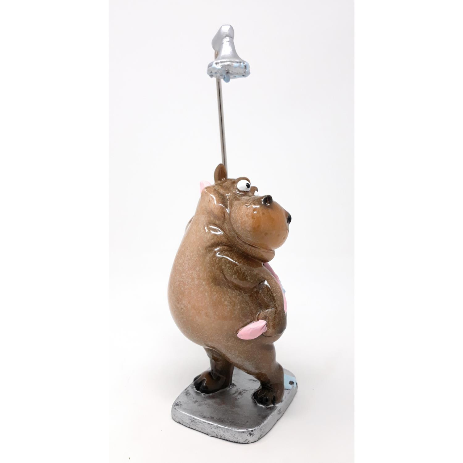 Eine braune, dickliche Figur eines Bären mit einem Glöckchen auf einem Stab. Der Bär hat eine freundliche Miene und steht auf einer grauen Basis.