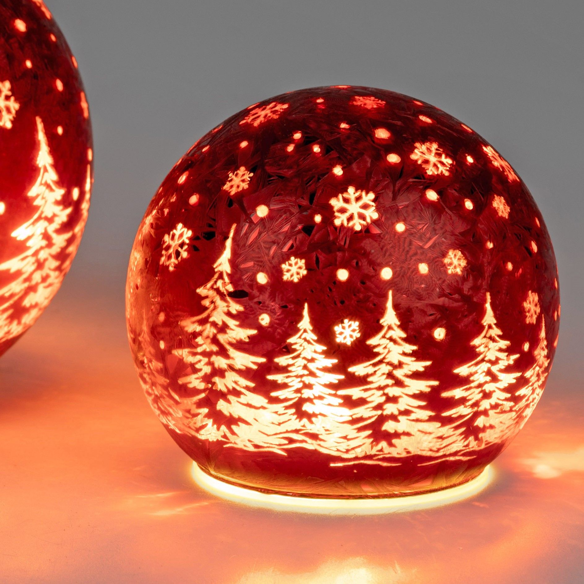 Runde, rote Glaskugeln mit weißen Weihnachtsbaum- und Schneeflockenmuster, beleuchtet von innen.
