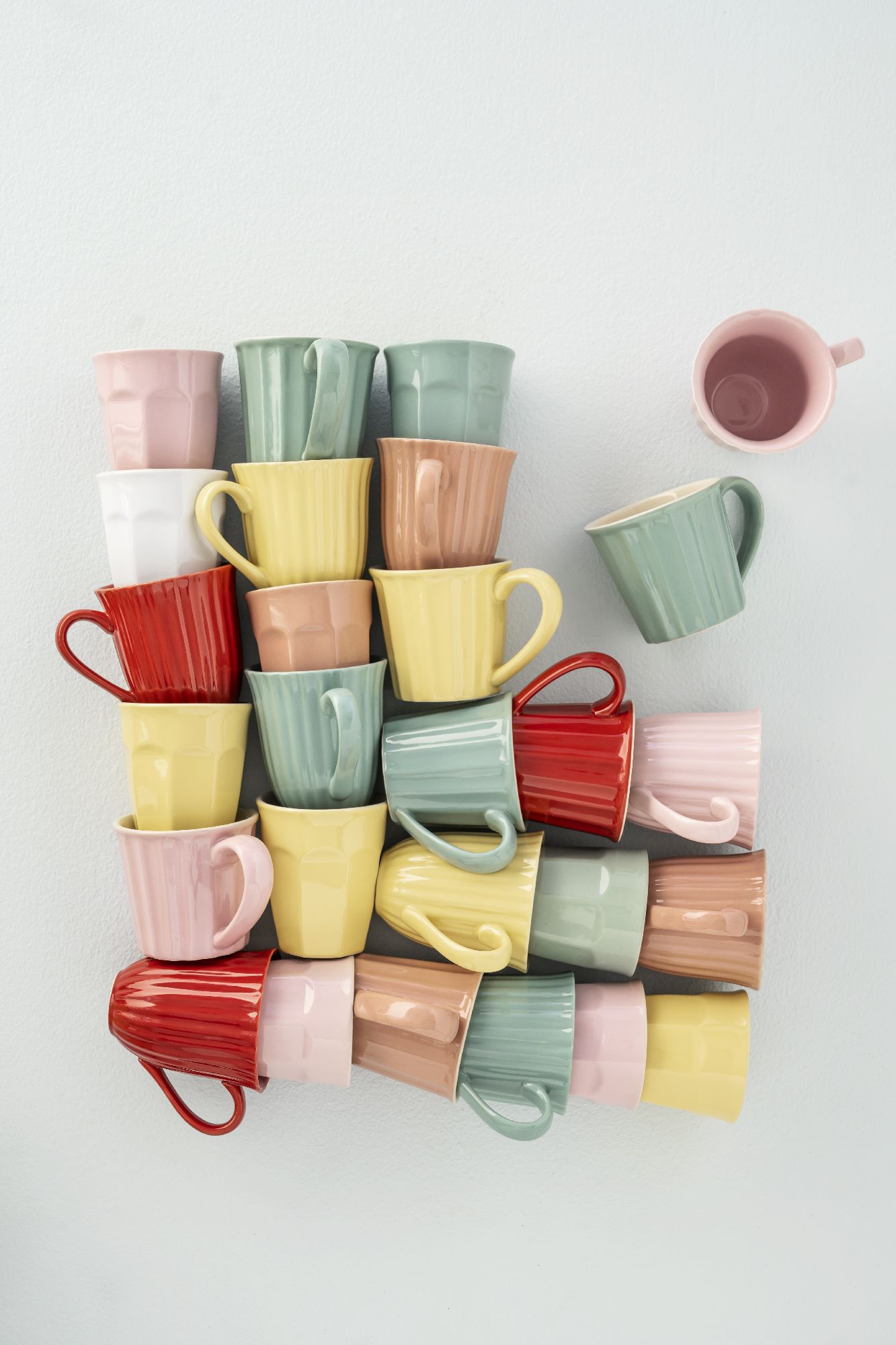 Bunte Tassen in verschiedenen Farben und Formen sind übereinander gestapelt, eine Tasse steht separat daneben.