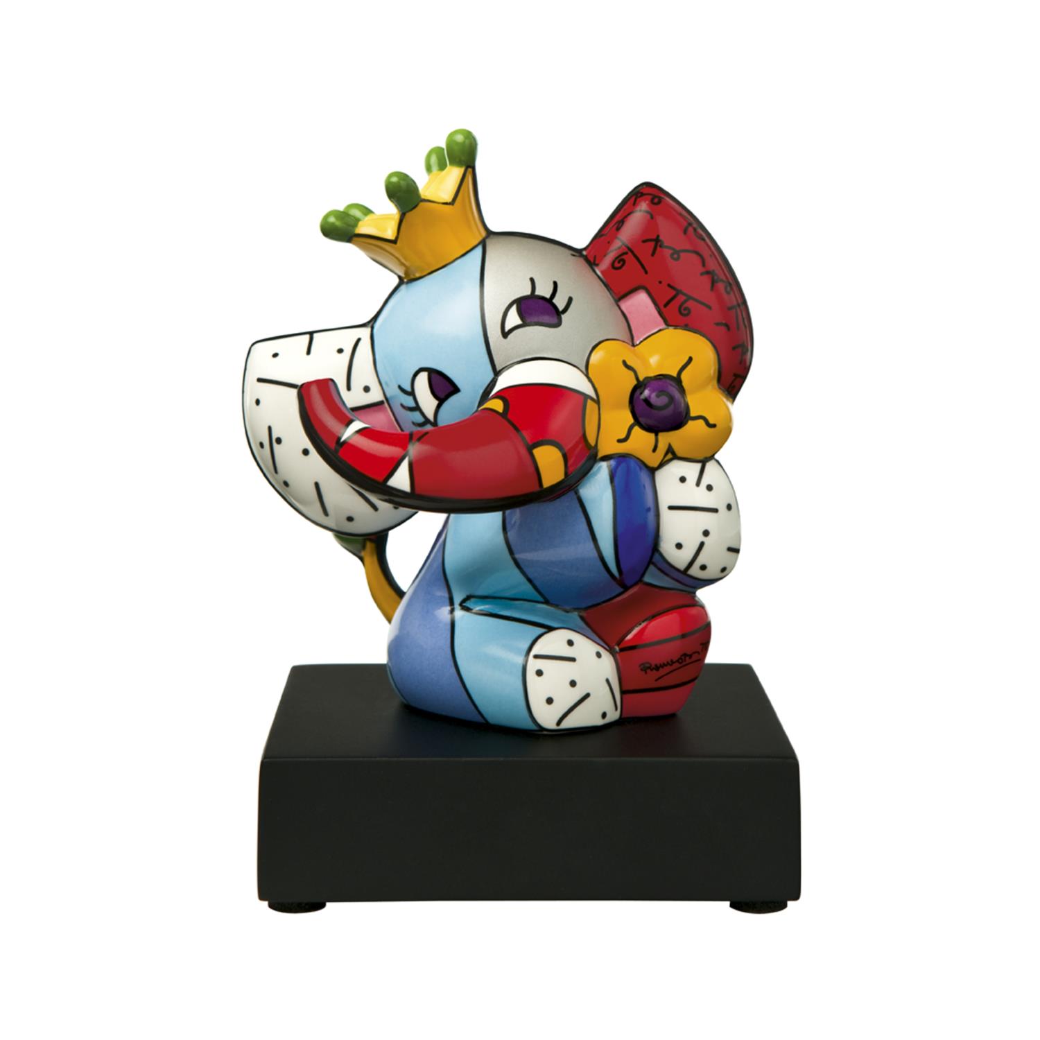 Bunte Elefantenfigur mit Krone, die eine Blume hält, auf schwarzem Sockel. Der Elefant hat große Ohren und einen lächelnden Gesichtsausdruck.