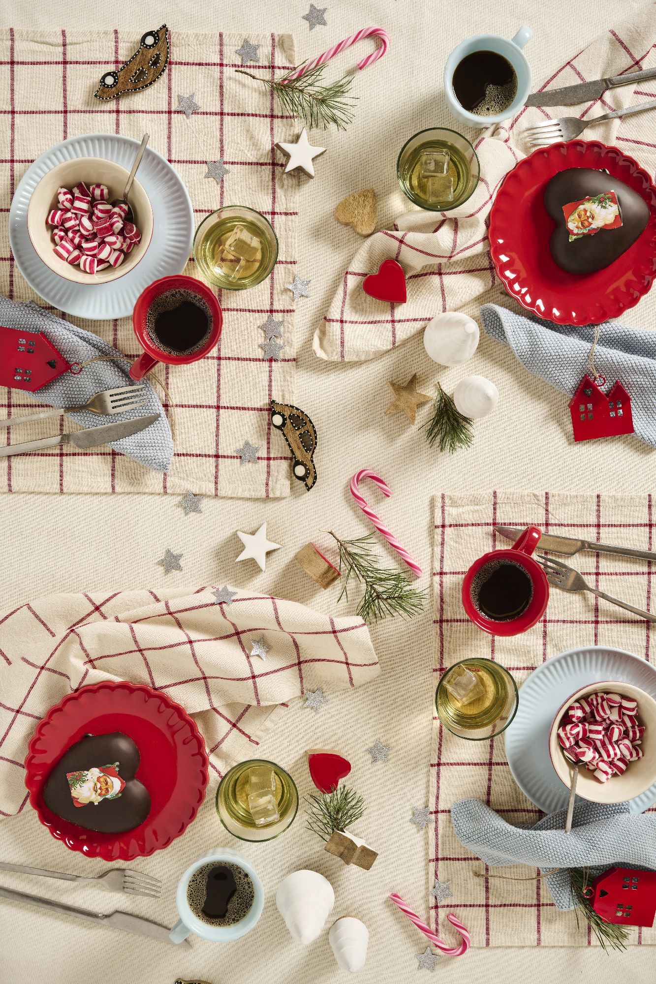 Tischgedeck mit zwei Tellern, Gläsern, Besteck und Dekoration. Süßigkeiten, Getränke und kleine Weihnachtsornamente sind sichtbar.