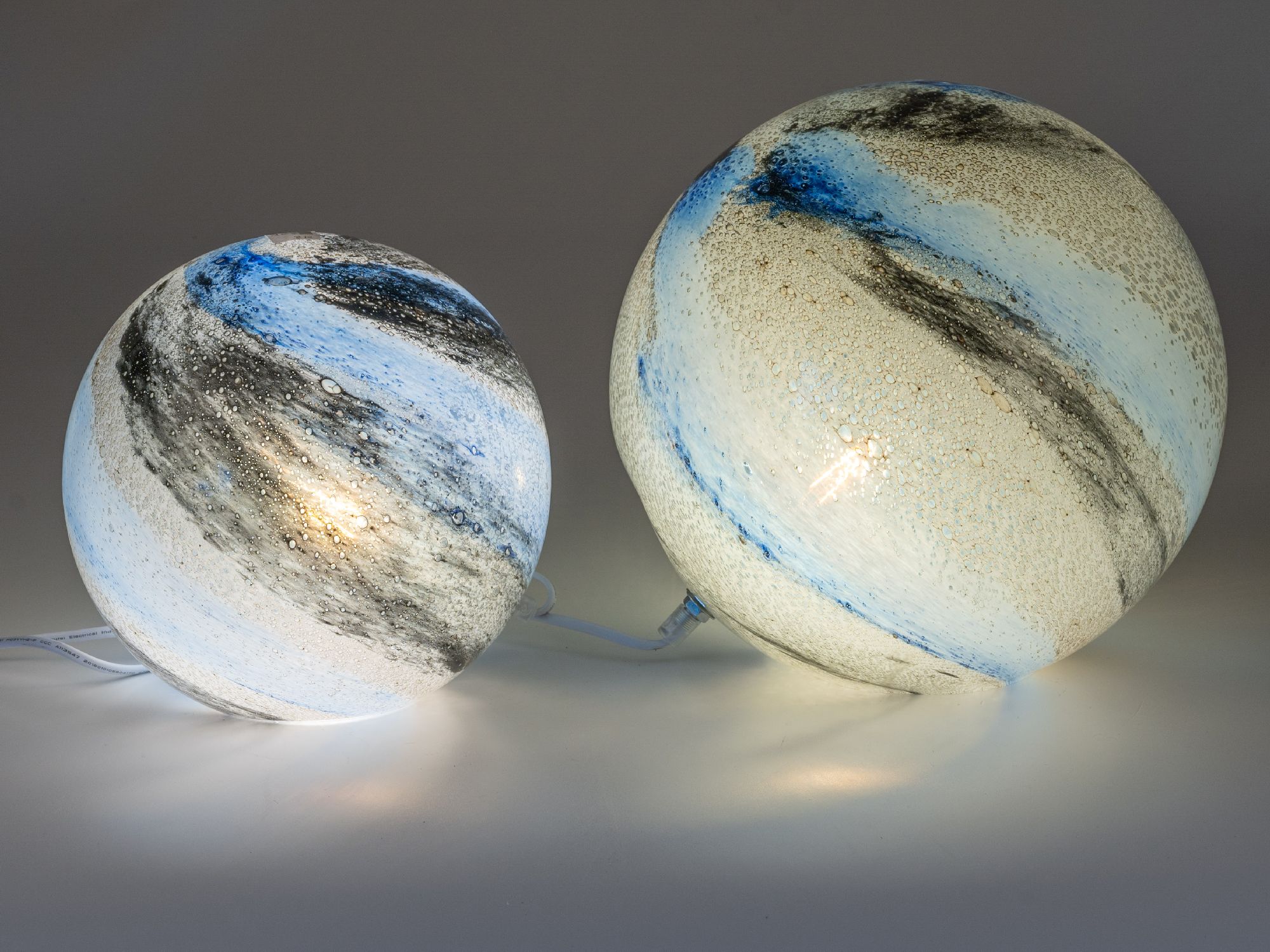 Zwei runde Lampen in verschiedenen Größen, mit blauen und schwarzen Mustern auf einer hellen Oberfläche, leuchten sanft.