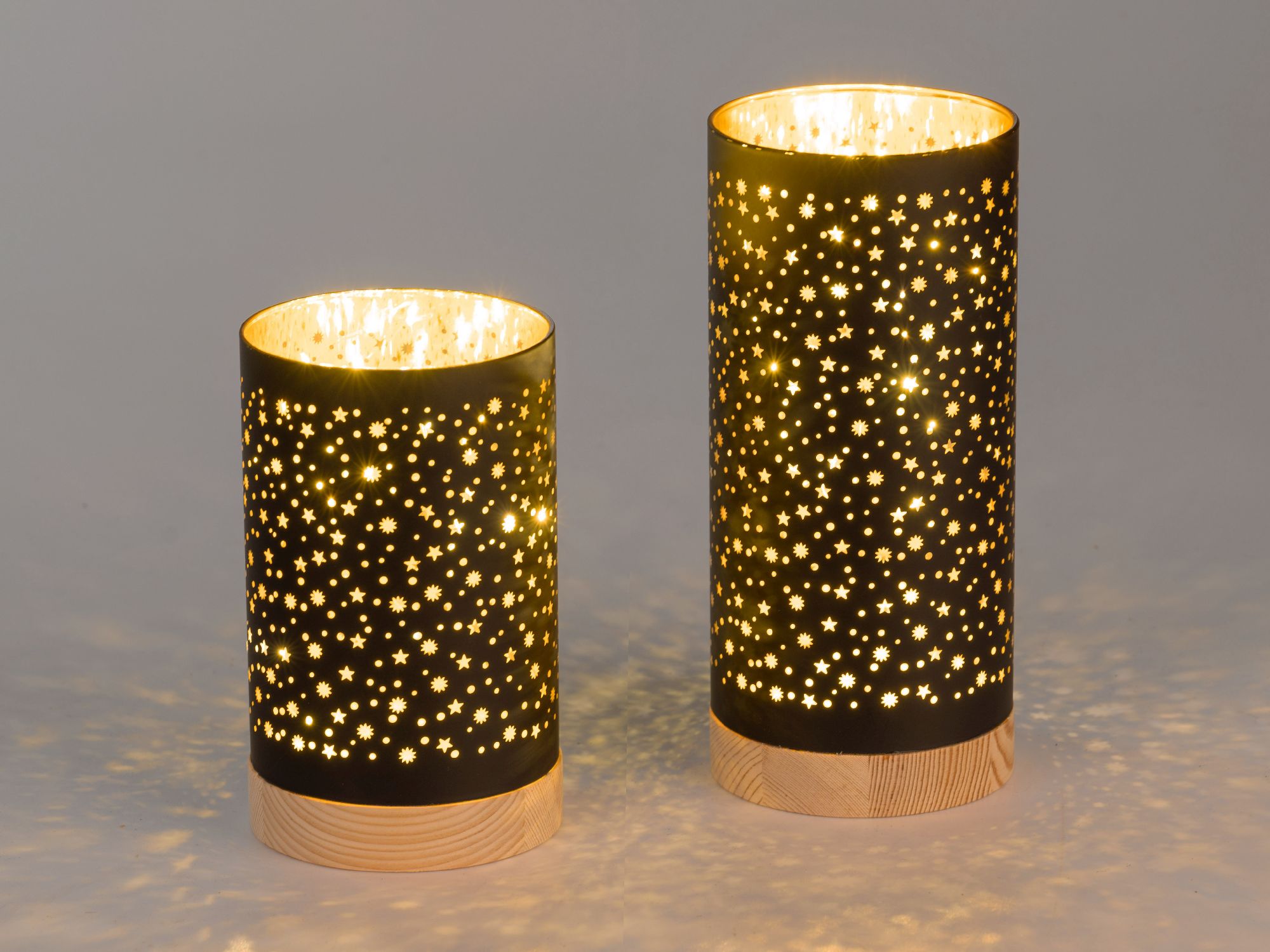 Zwei schwarze Lampen in Zylinderform mit Sternmotiven auf Holzsockel