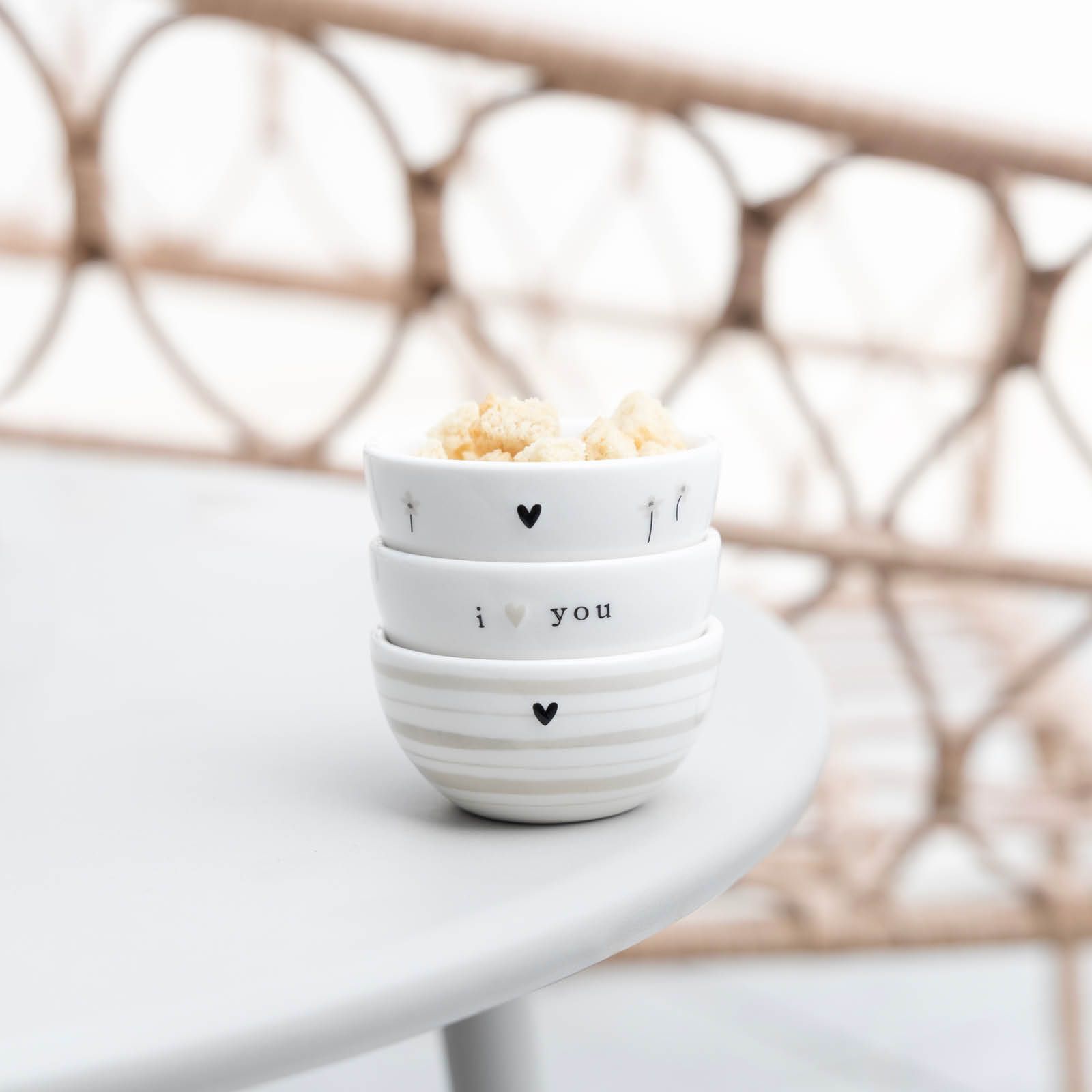 Drei gestapelte Schalen aus Keramik mit verschiedenen Mustern und Aufschriften, gefüllt mit Snacks, auf einem Tisch.