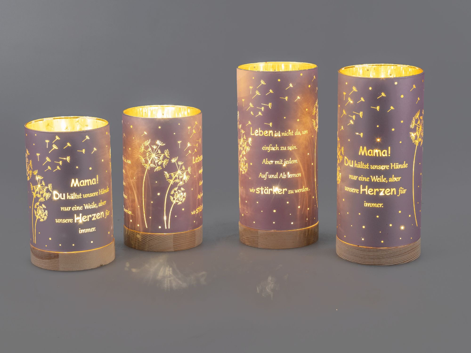 Vier dekorative Kerzenhalter mit Sprüchen und Pusteblumen-Motiven auf lila Hintergrund. Holzsockel, warmes Licht.