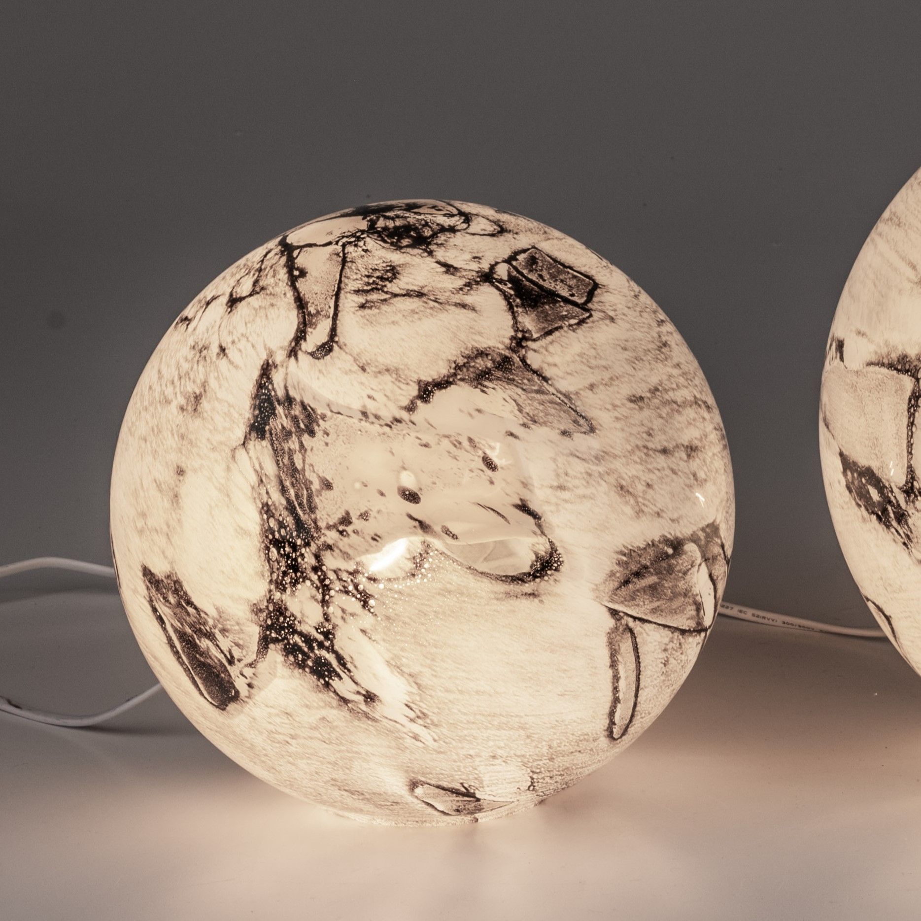 Zwei runde Lampen aus transparentem Material mit schwarz-weißen Mustern auf der Oberfläche, auf einem hellen Untergrund.