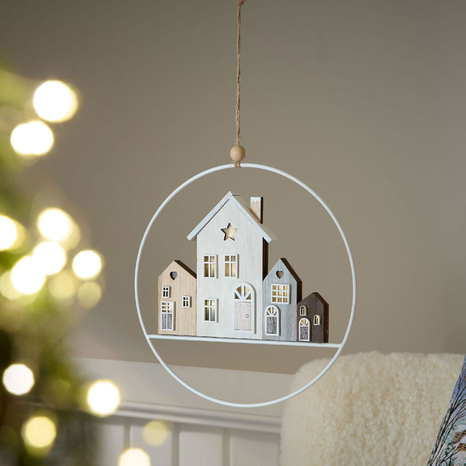 Hängende Dekoration aus Holz in Form von Häusern, umgeben von einem weißen Ring. Im Hintergrund unsc