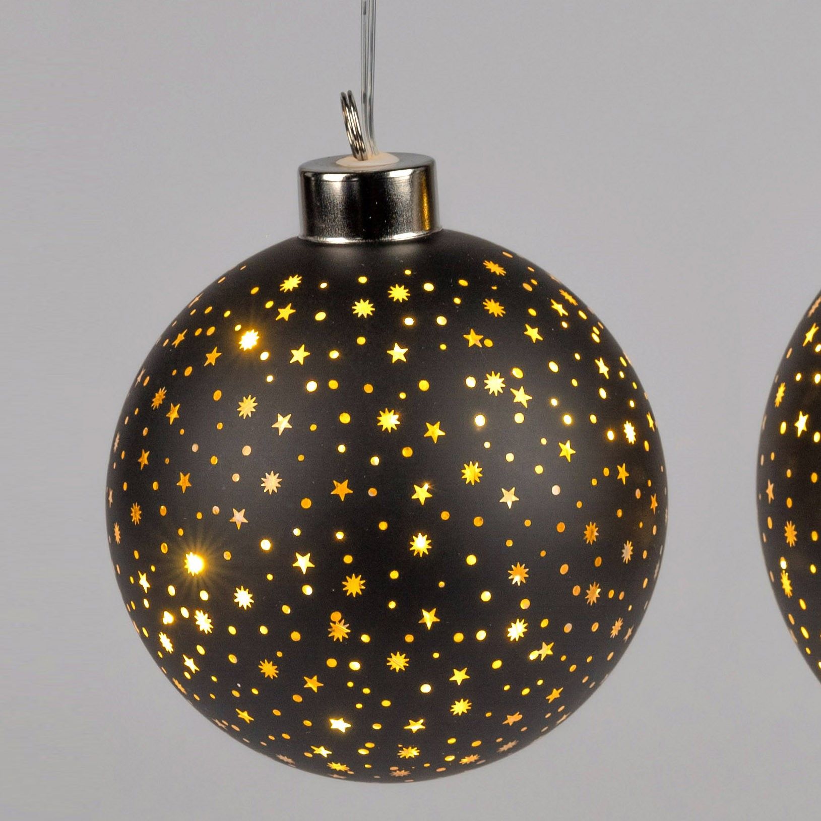 Schwarze Weihnachtskugel mit goldenen Sternen und Punkten, die Licht durchlässt, hängt an einem silb