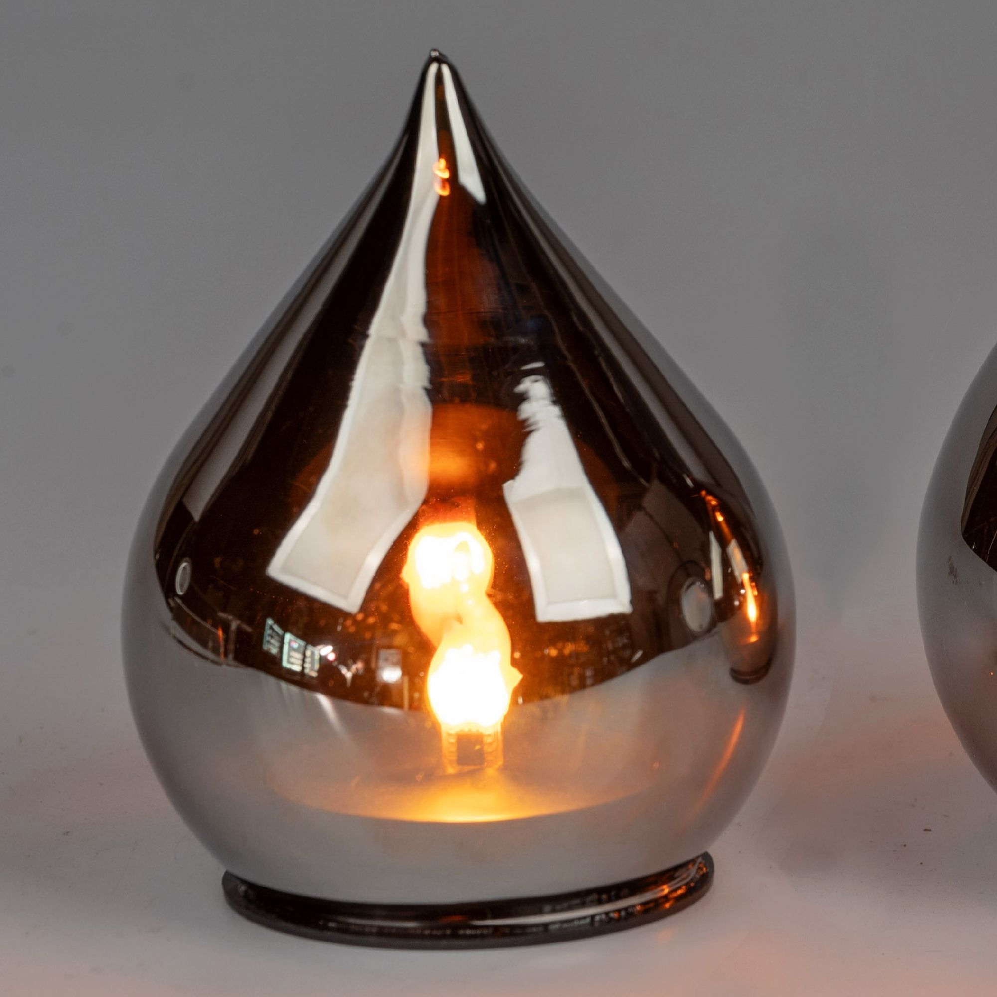 Zwei lampenförmige Objekte in Tropfenform, eines leuchtet orange, mit reflektierender, metallischer