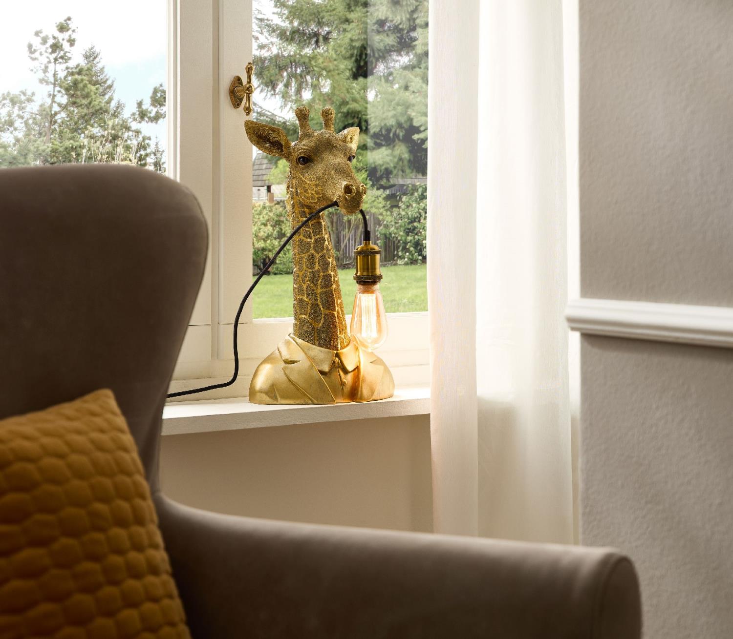 Eine Giraffenlampe steht auf einer Fensterbank. Im Hintergrund sind Bäume und ein Garten sichtbar. E