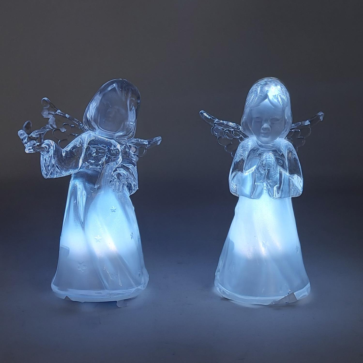 Zwei durchsichtige Engel aus Glas mit leuchtenden Körpern stehen nebeneinander vor einem dunklen Hin
