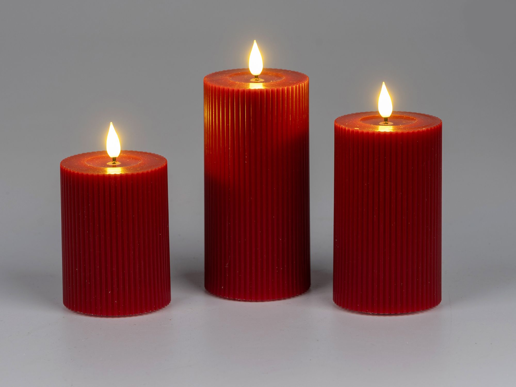 Drei rote, geriffelte Kerzen mit Flammen stehen auf einem hellen Hintergrund. Die Kerzen sind unters