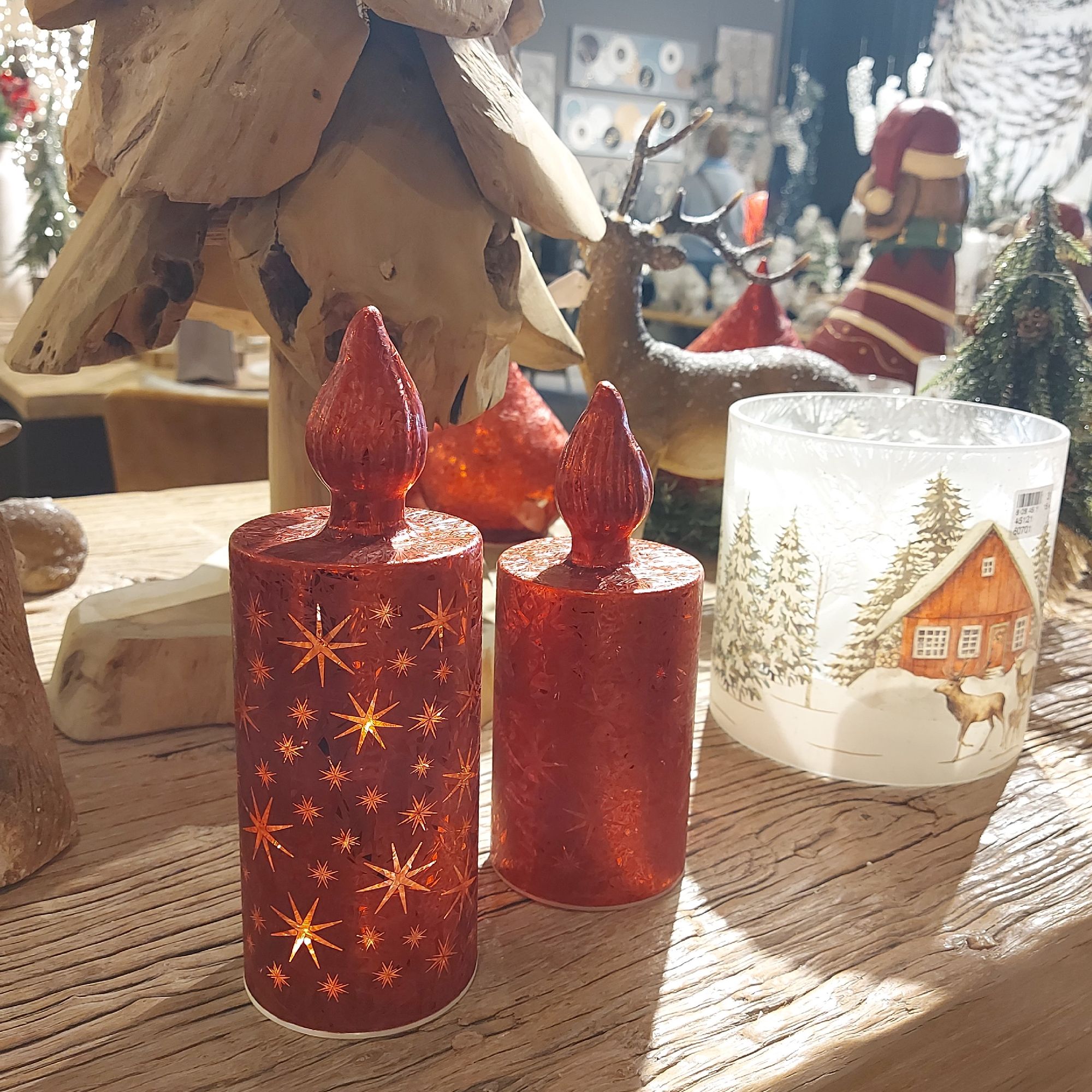 Zwei rote Kerzen mit Sternenmustern stehen auf einem Holztisch, umgeben von weiteren dekorativen Obj