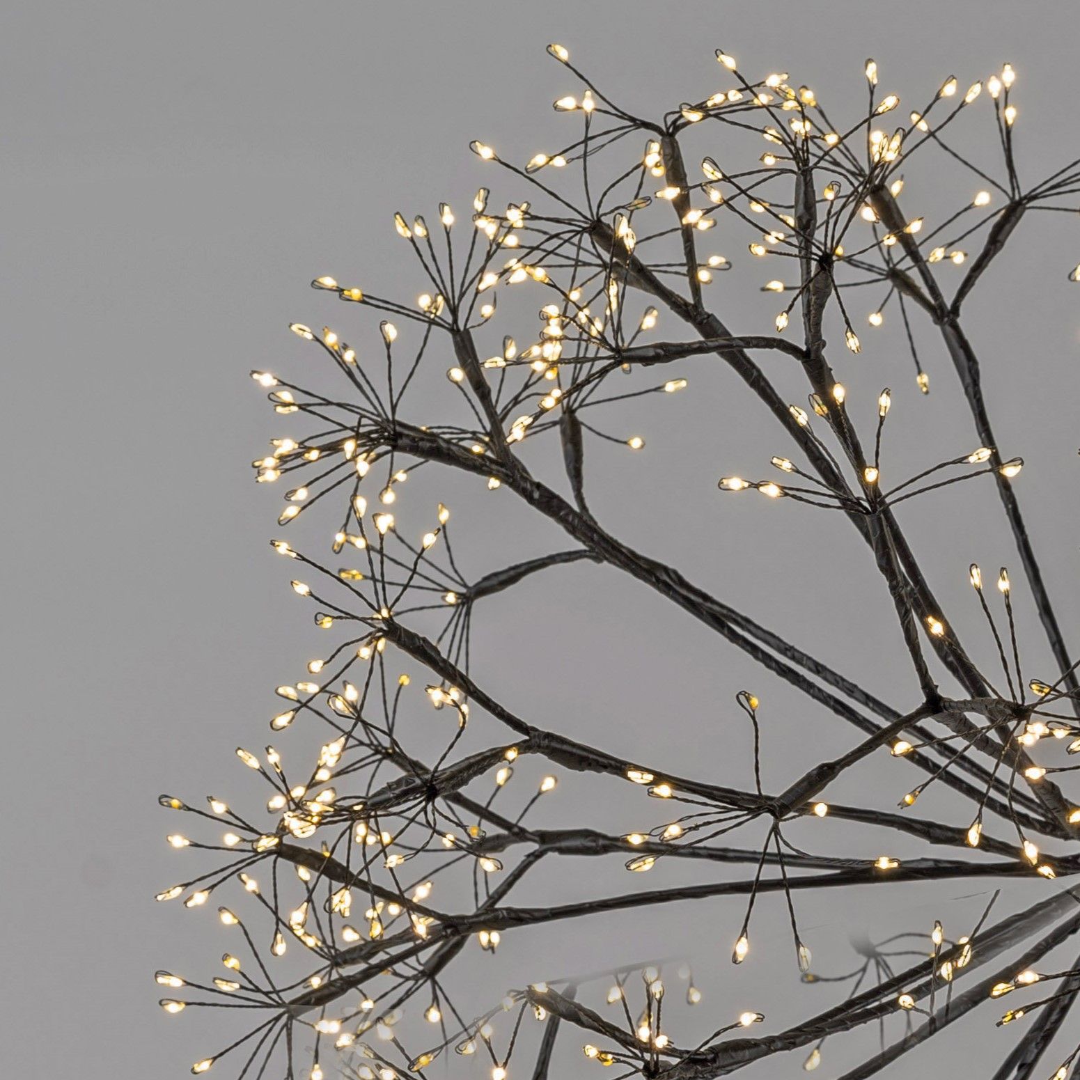 Eine dekorative Leuchte mit dünnen, verzweigten Ästen, die mit kleinen, warmweißen Lichtern besetzt
