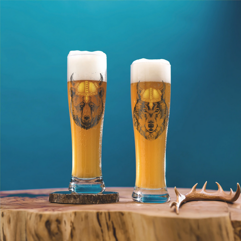 Zwei Gläser Bier mit Tiermotiven stehen auf einem Holzuntergrund. Im Hintergrund ist eine blaue Wand sichtbar.
