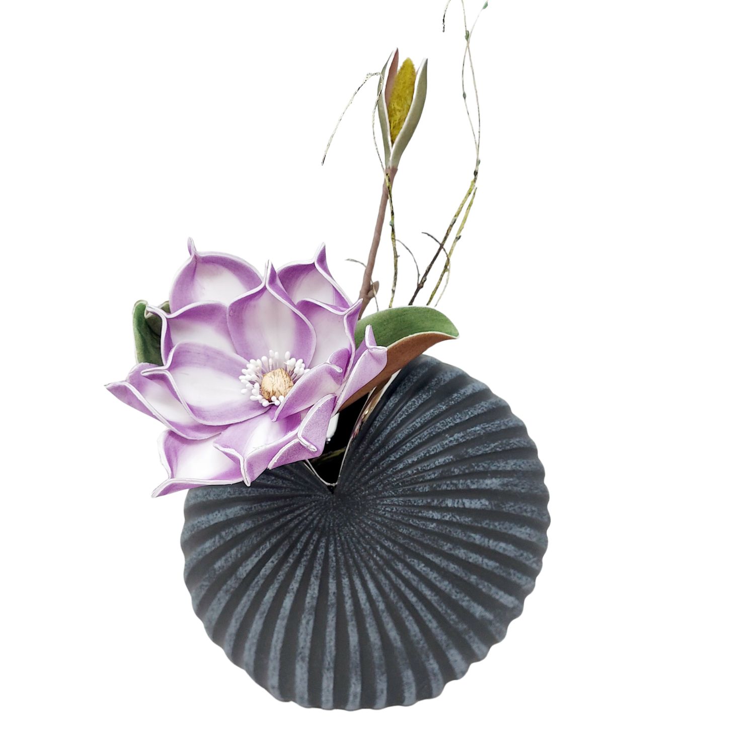 Lila-weiße Blüte mit Blättern und Zweigen in runder, gerillter schwarzer Vase