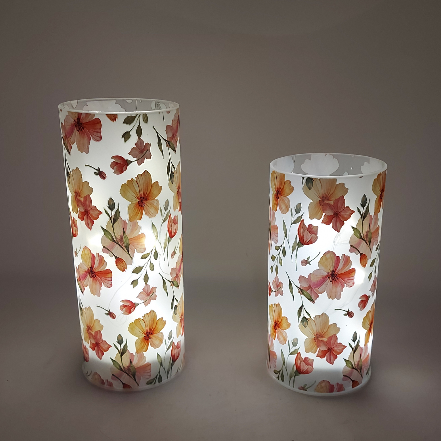 zwei weiß transparenter Glaszylinder mit Blumenmotiven beleuchtet