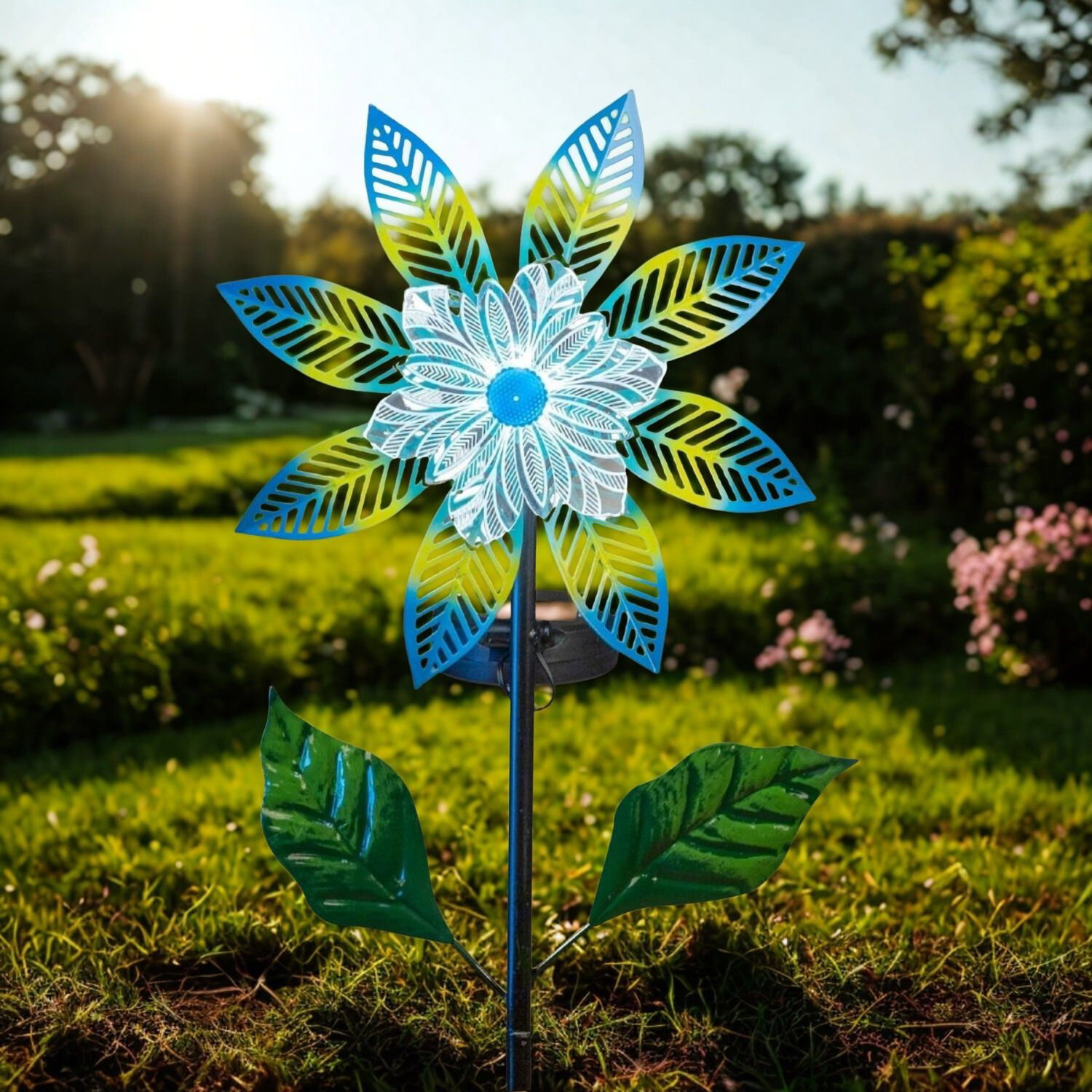 Bunte Gartenwindmühle in Blütenform mit blauen und grünen Blättern auf Rasen bei Sonne